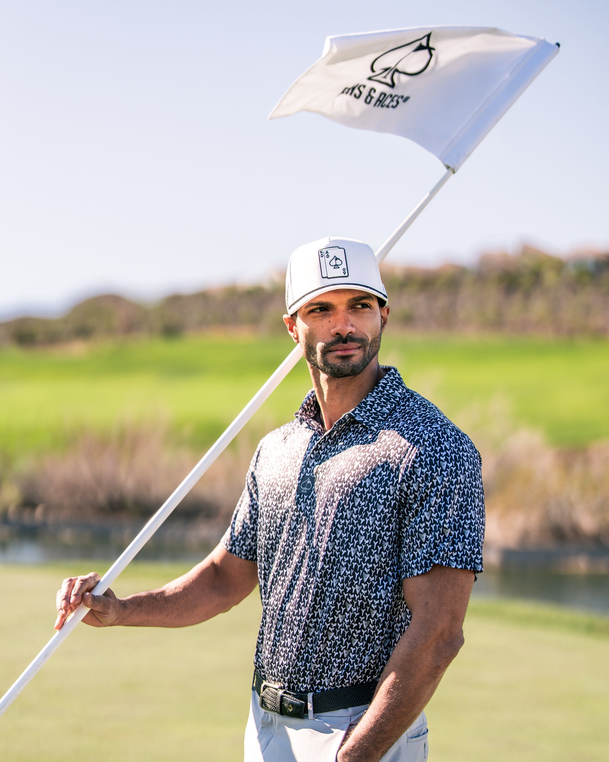 A golfer in a stylish patterned shirt holds a flag on the course, showcasing bold golf apparel and confidence.