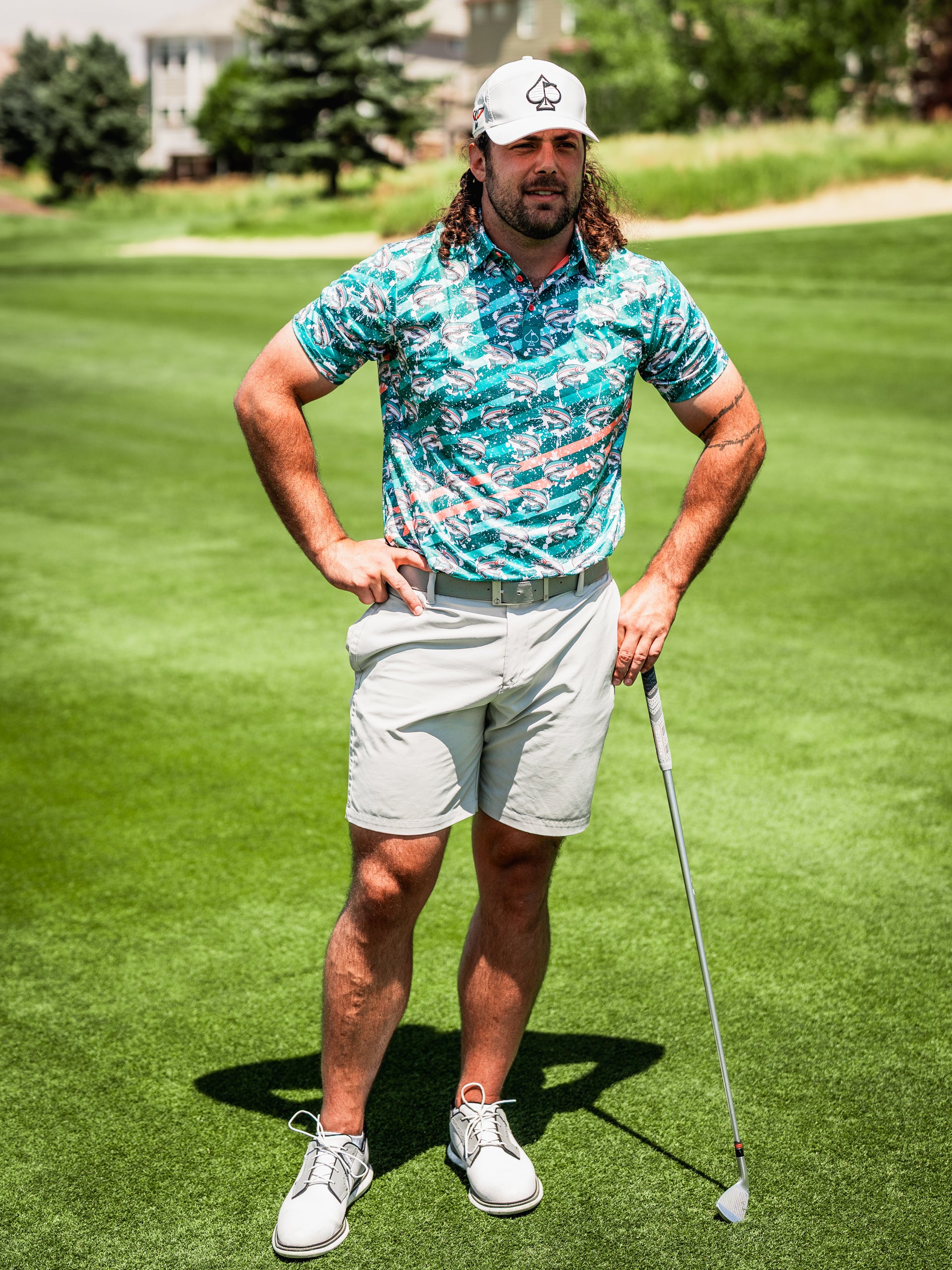 A golfer stands confidently on the course, wearing a vibrant Trout Splatter shirt and light shorts, ready to swing.