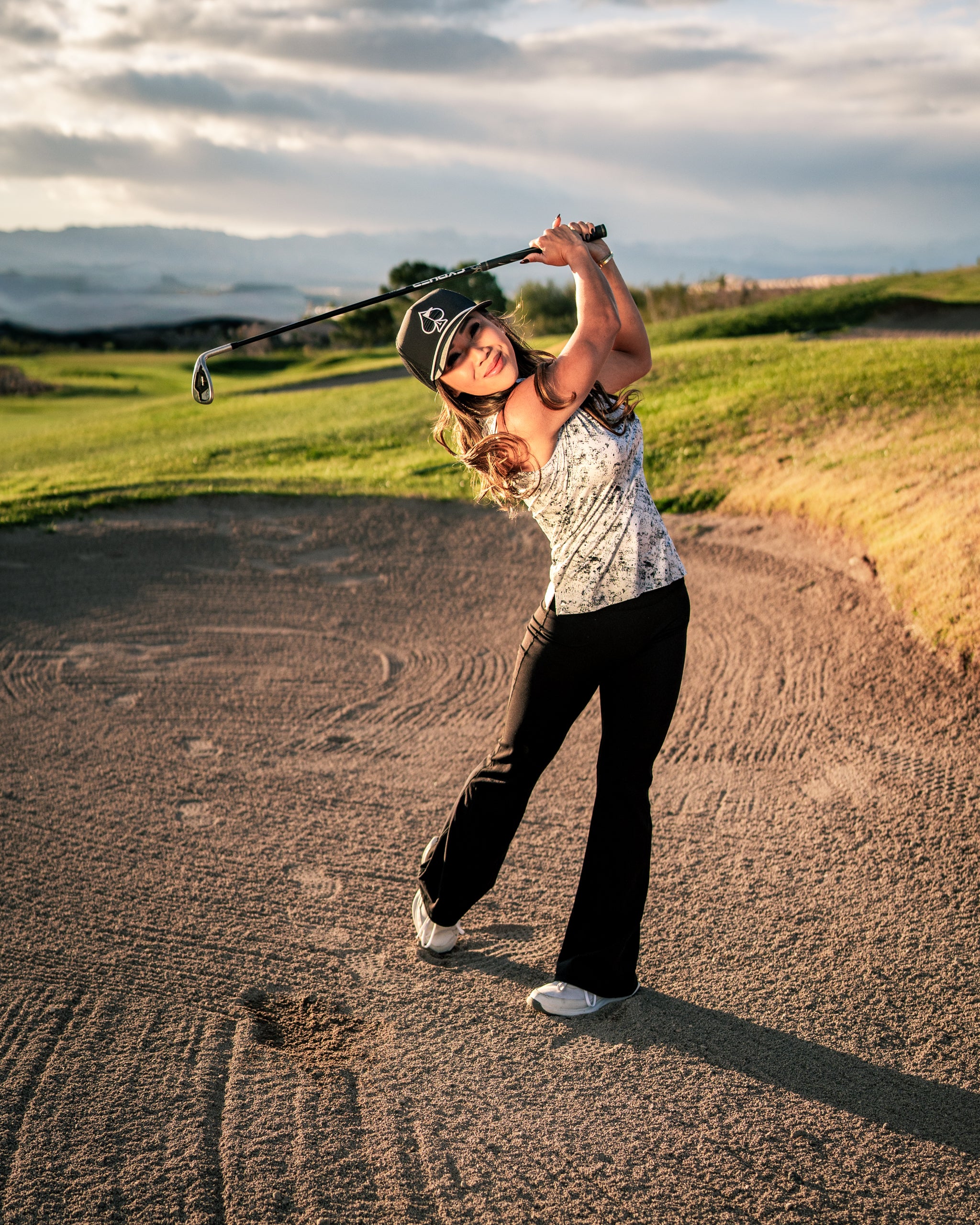 Woman in stylish golf apparel swings a club on a sandy course, showcasing confidence and bold style.