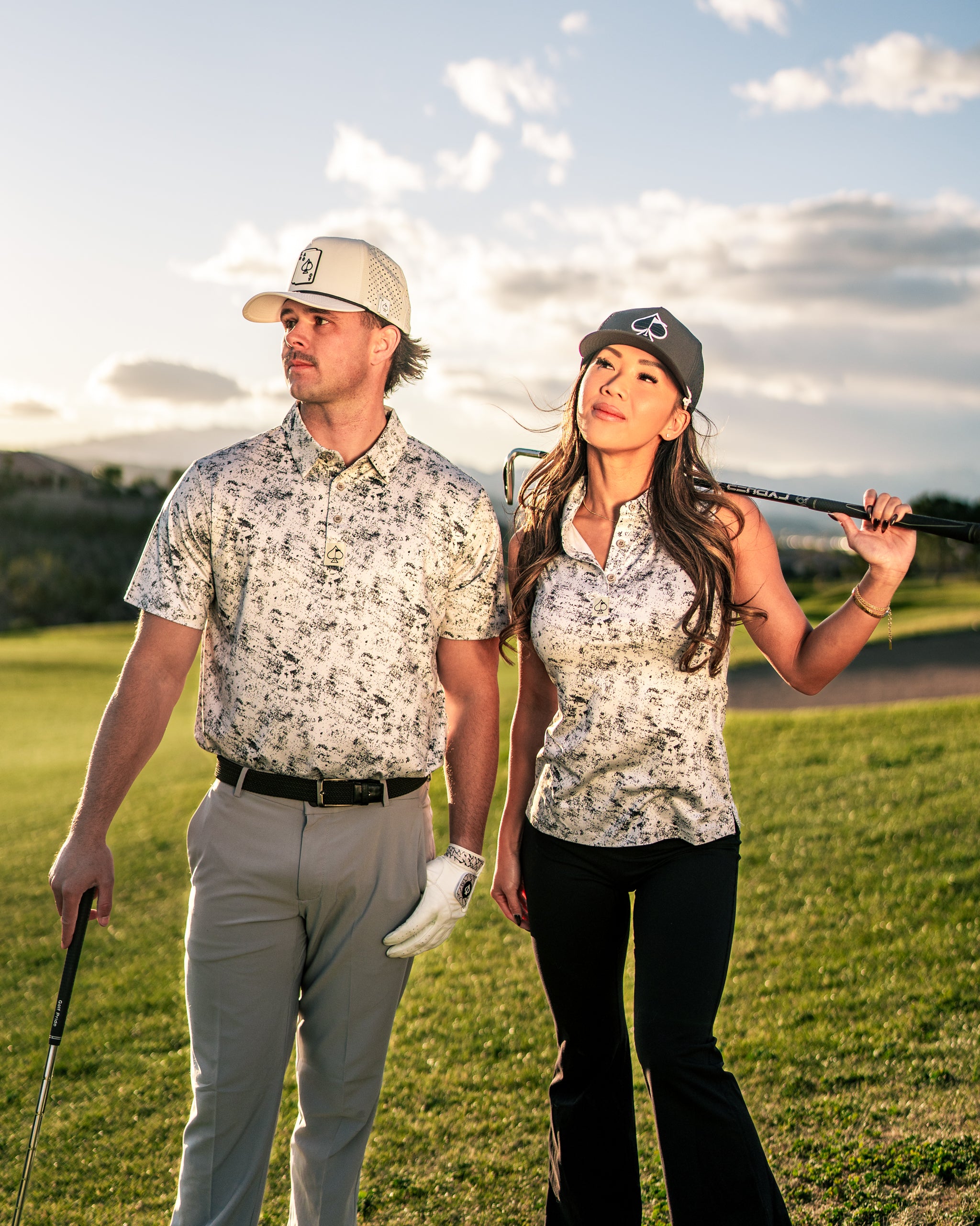 Stylish couple on a golf course wearing matching white noise patterned golf apparel, showcasing a modern and bold look.