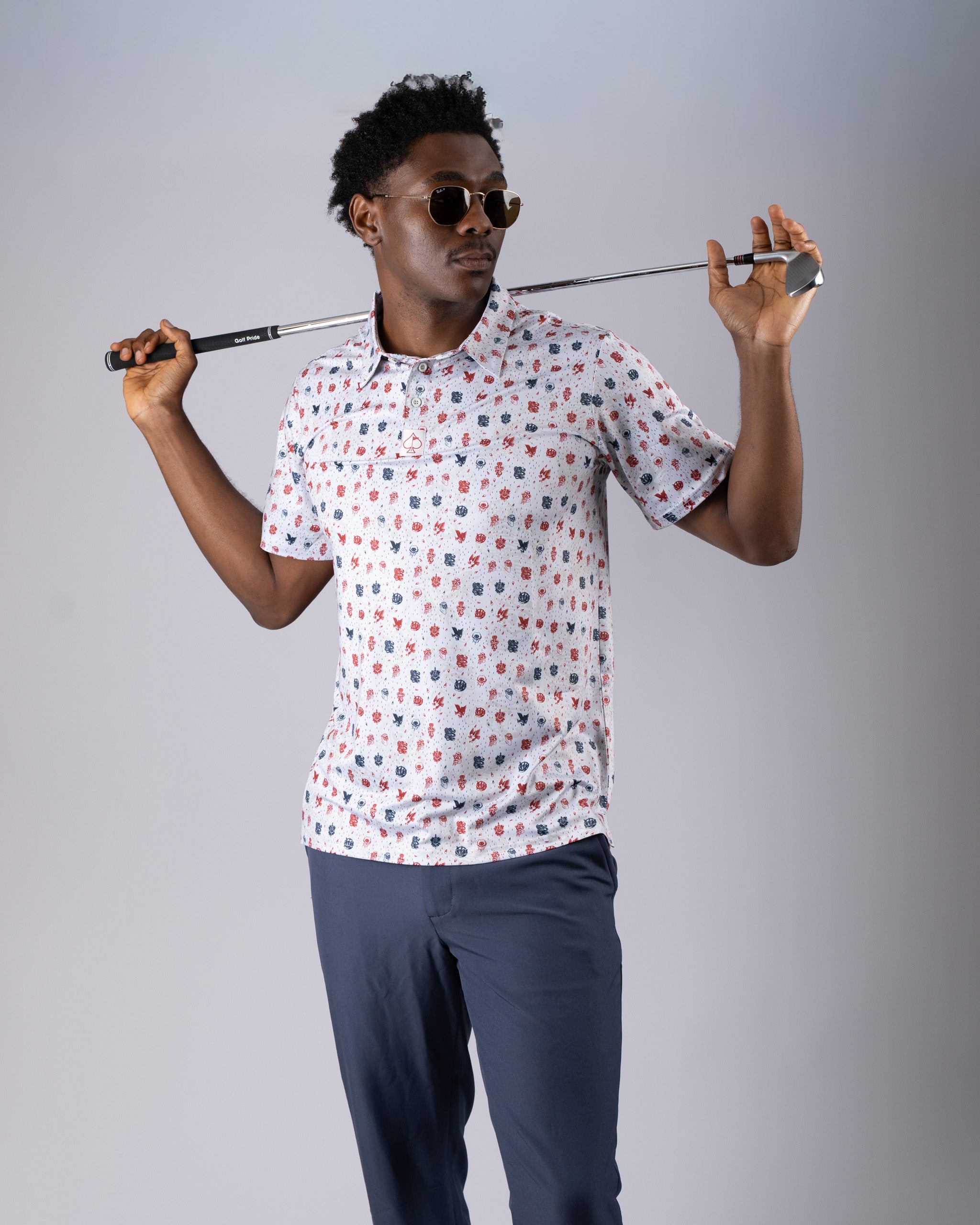 Model wearing the American Traditional golf shirt featuring a colorful floral pattern, holding a golf club and wearing sunglasses.