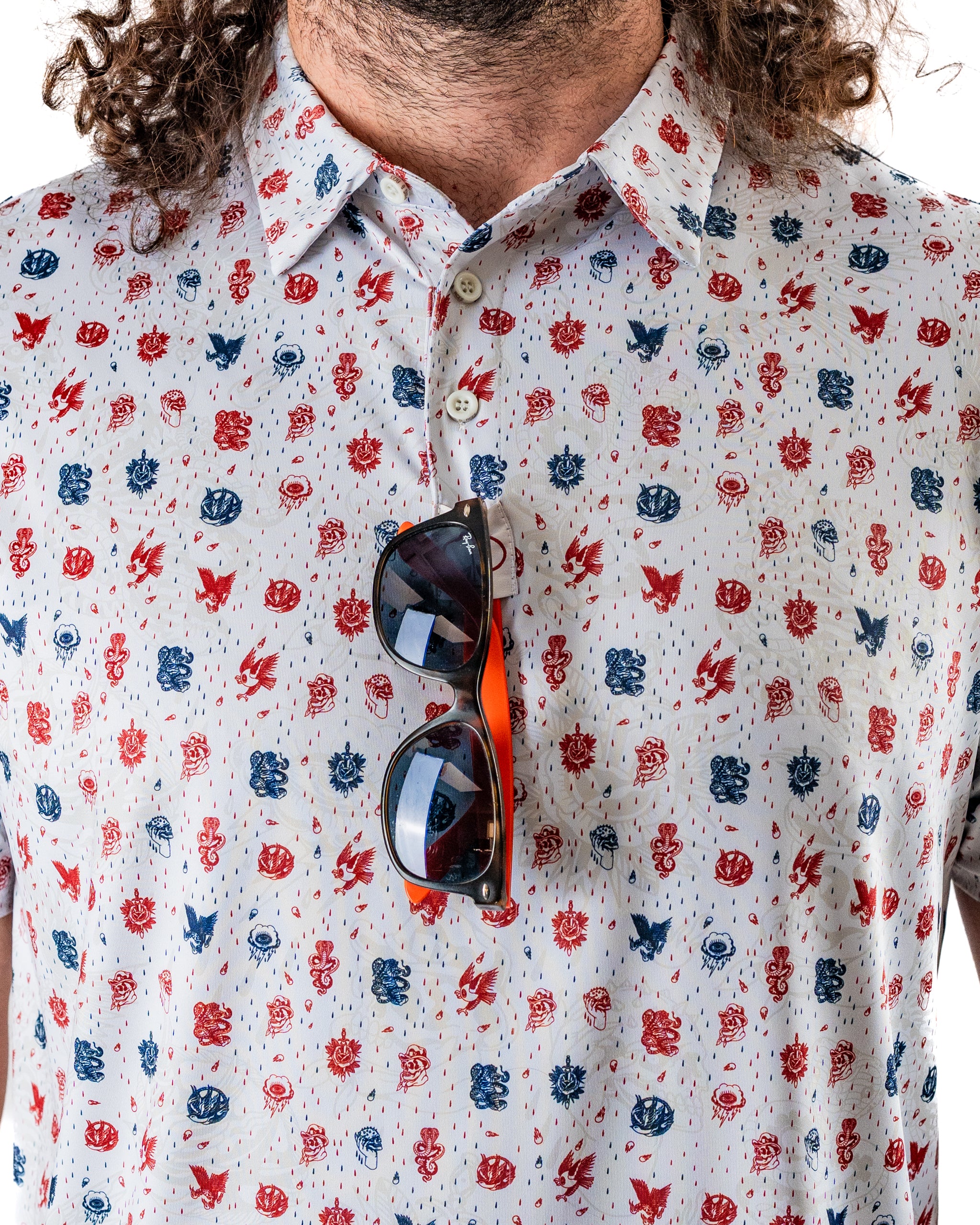 Bold golf shirt featuring an American traditional print with red and blue designs, paired with stylish sunglasses.
