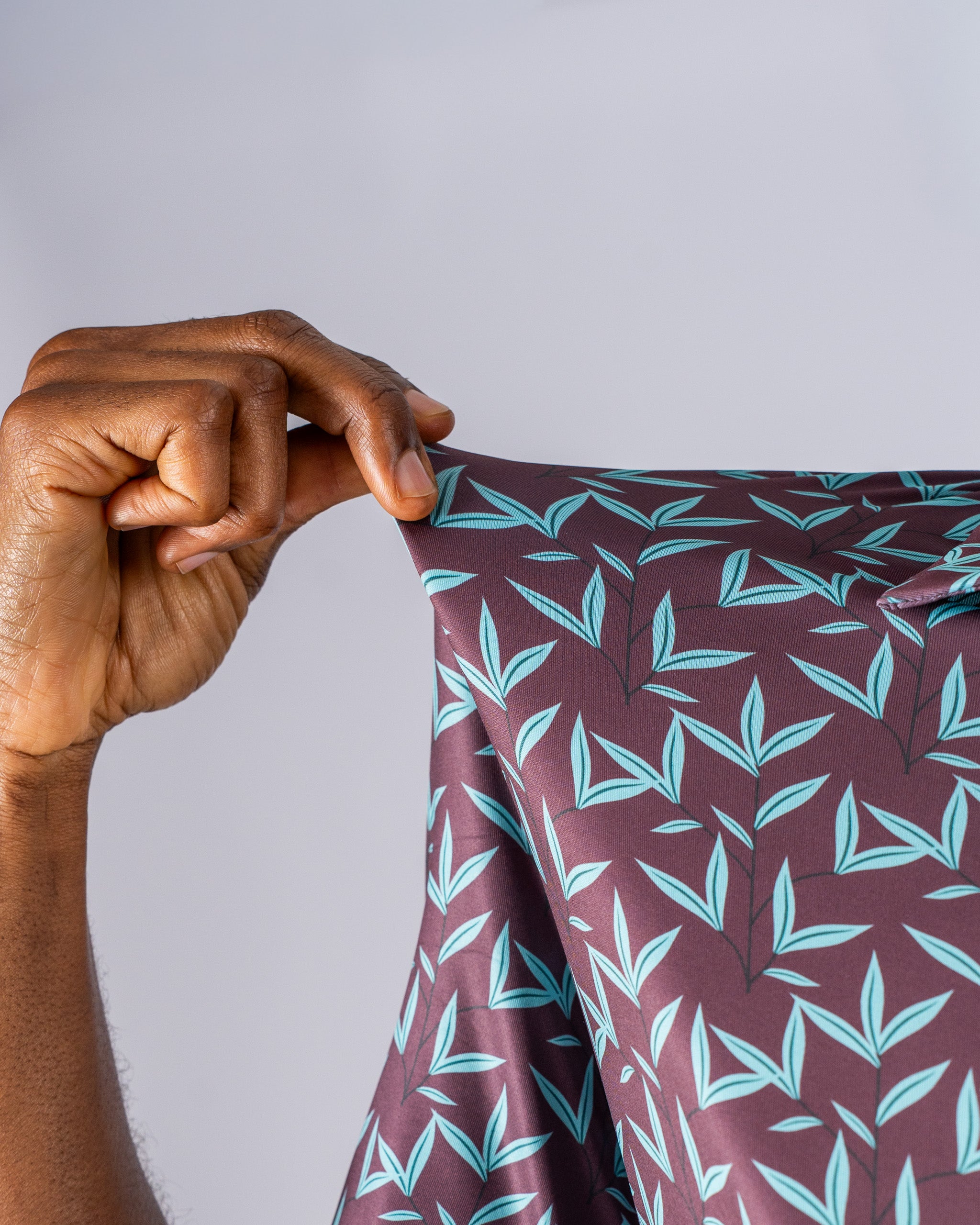Close-up of a hand holding a stretchable fabric featuring a cocoa brown background with teal leaf patterns, showcasing its texture.