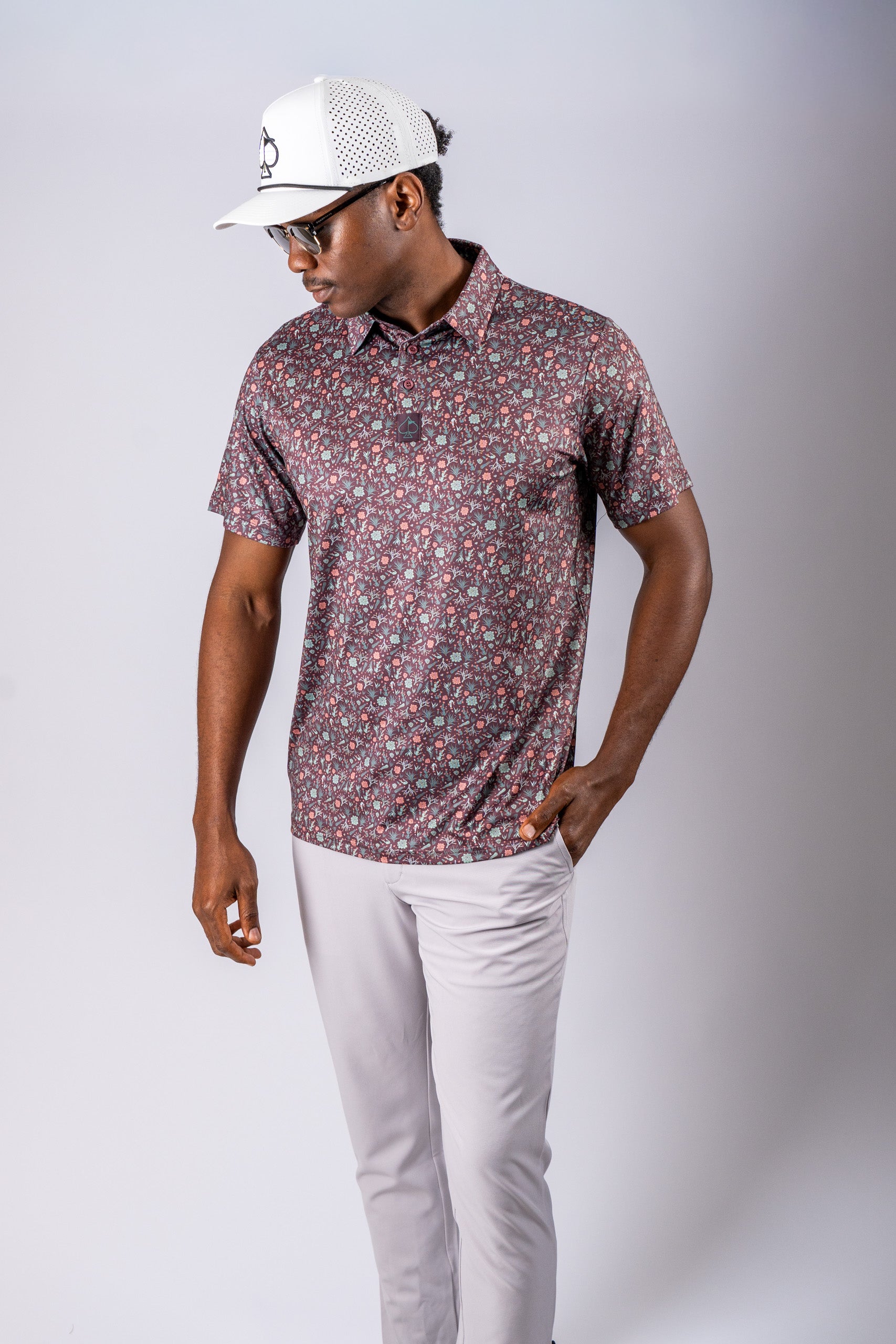 Stylish golfer wearing a Desert Sage patterned polo shirt and a white cap, showcasing bold golf apparel.