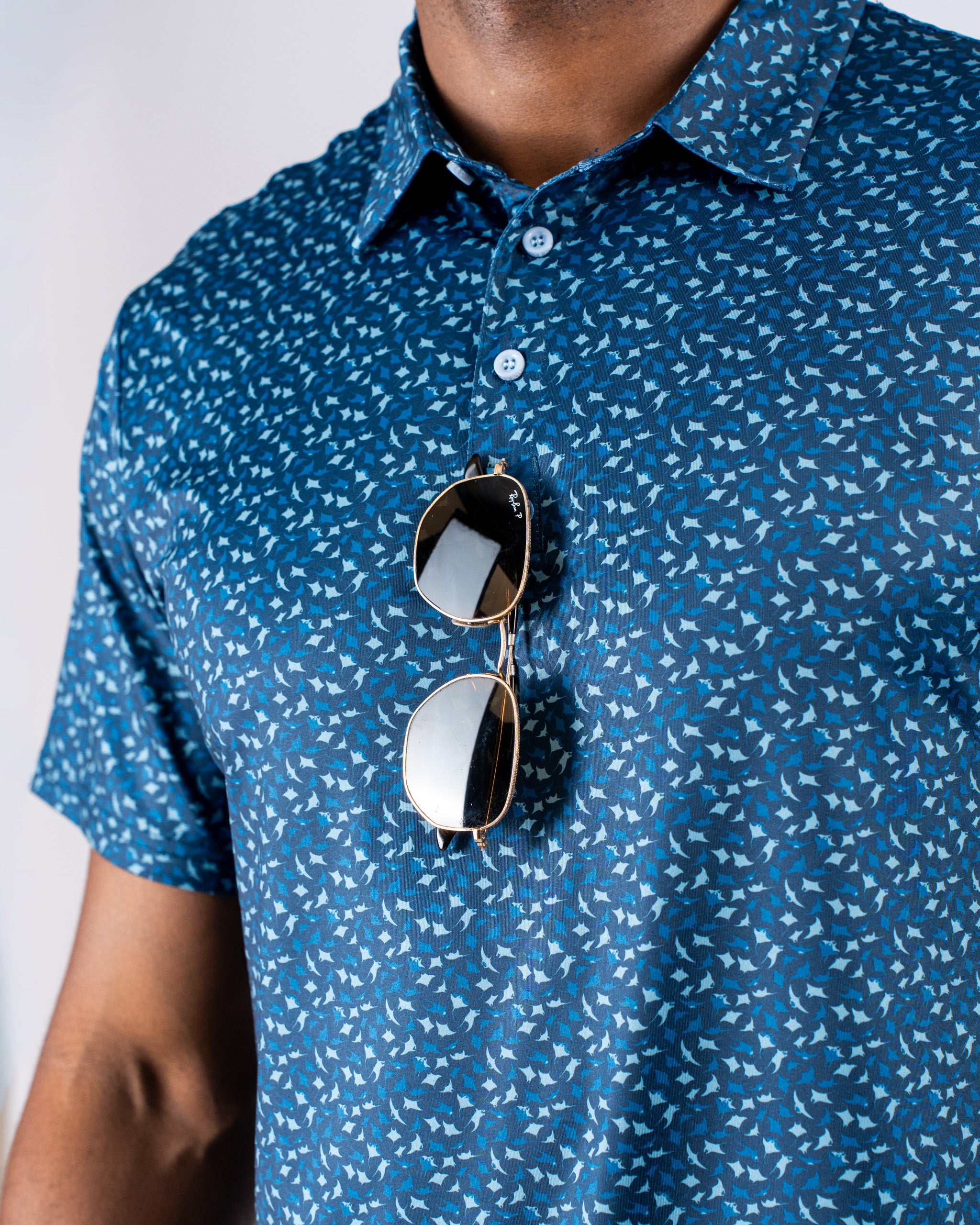 Men's Manta Ray golf polo in blue with a unique pattern, featuring sunglasses casually draped over the collar.