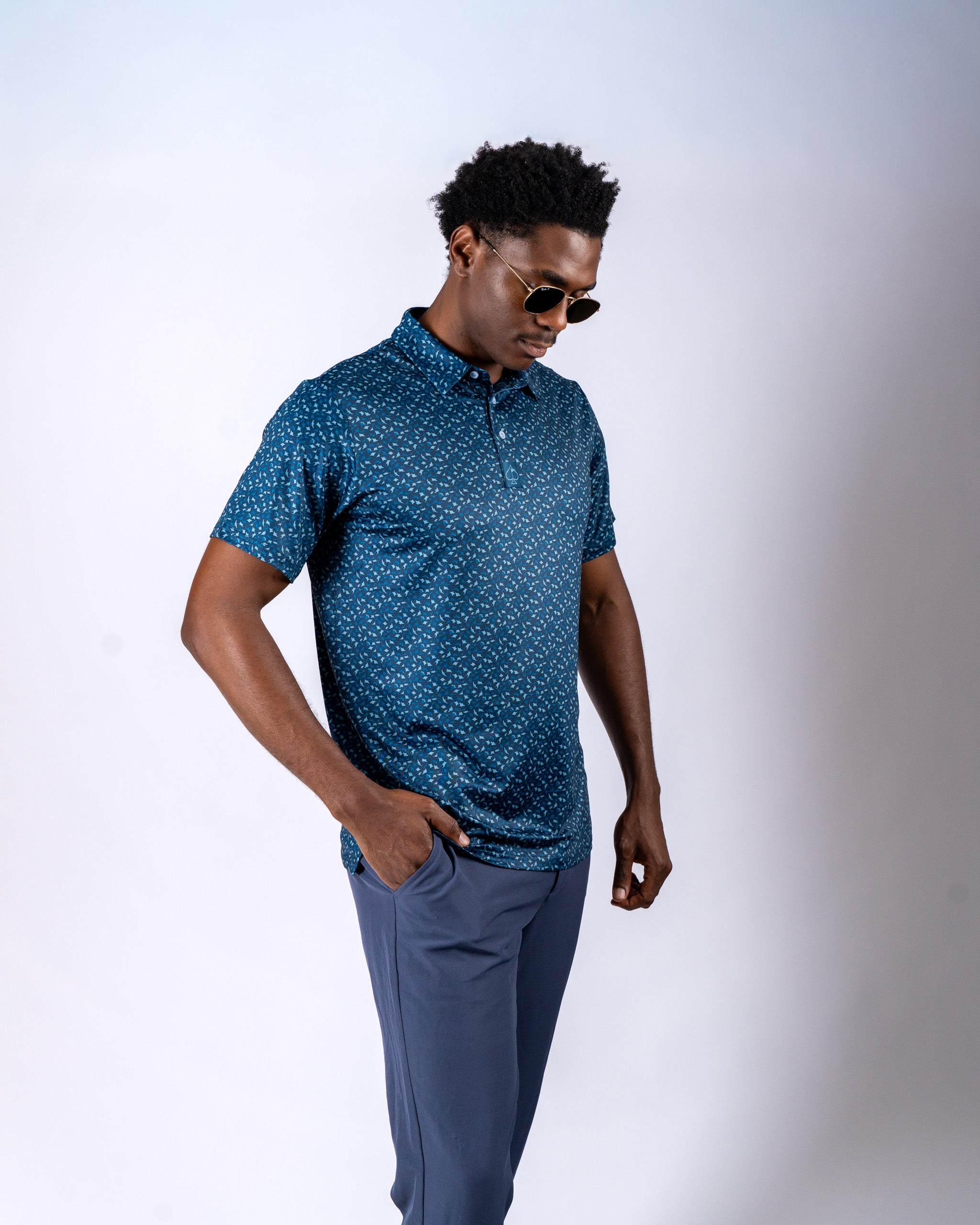 Men's Manta Ray golf polo in blue with a unique pattern, paired with stylish sunglasses and tailored pants.