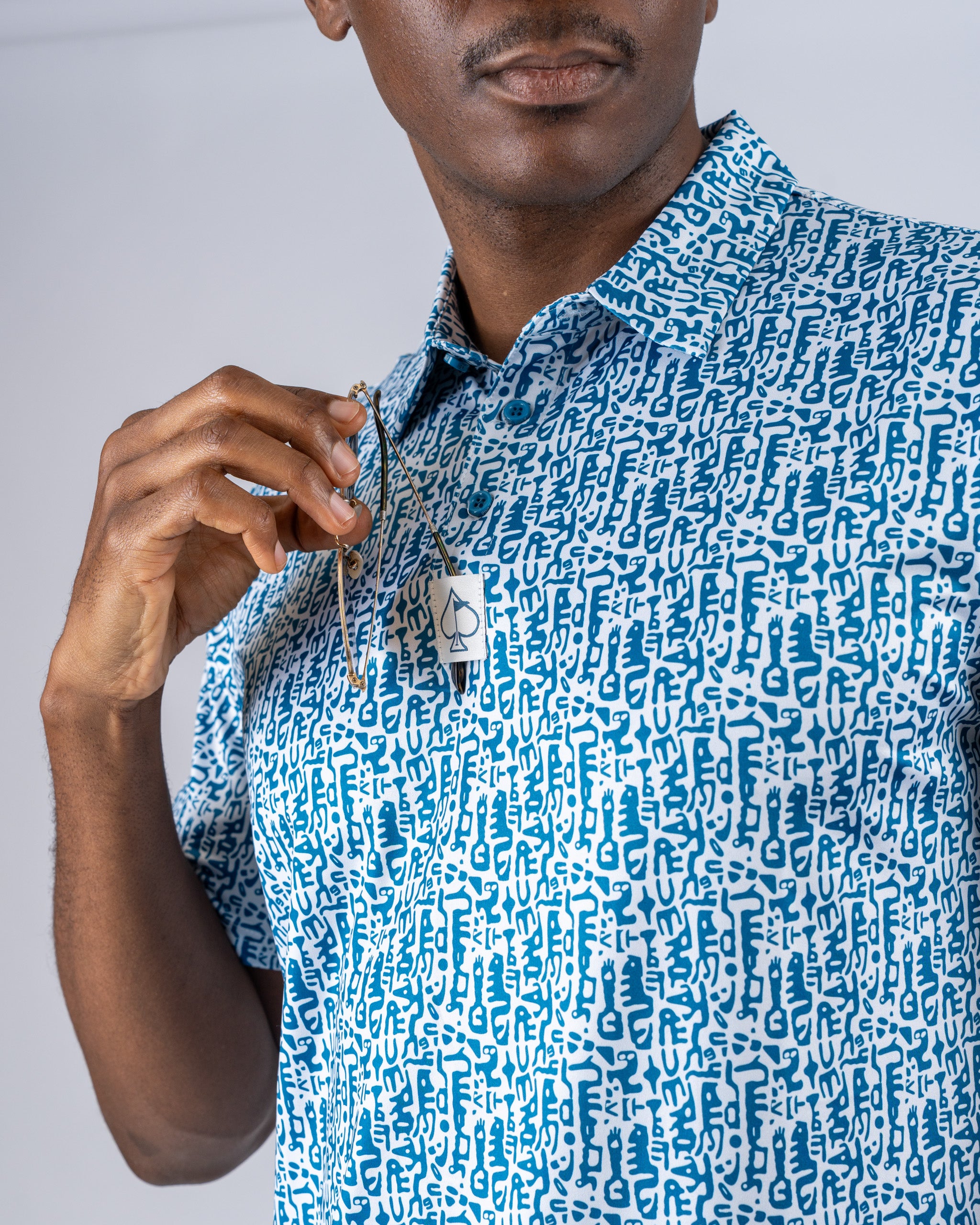 A man holds golf tees while wearing a blue and white patterned shirt featuring a maze-like design.
