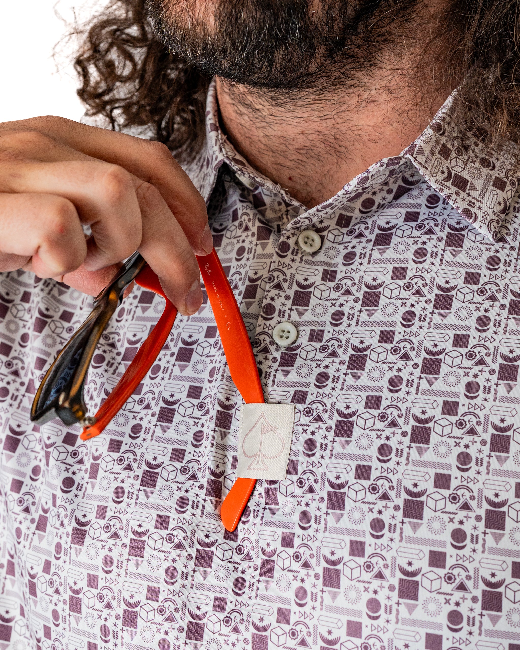 Man holding sunglasses against a patterned shirt featuring retro golf-themed designs, showcasing a stylish golf accessory.