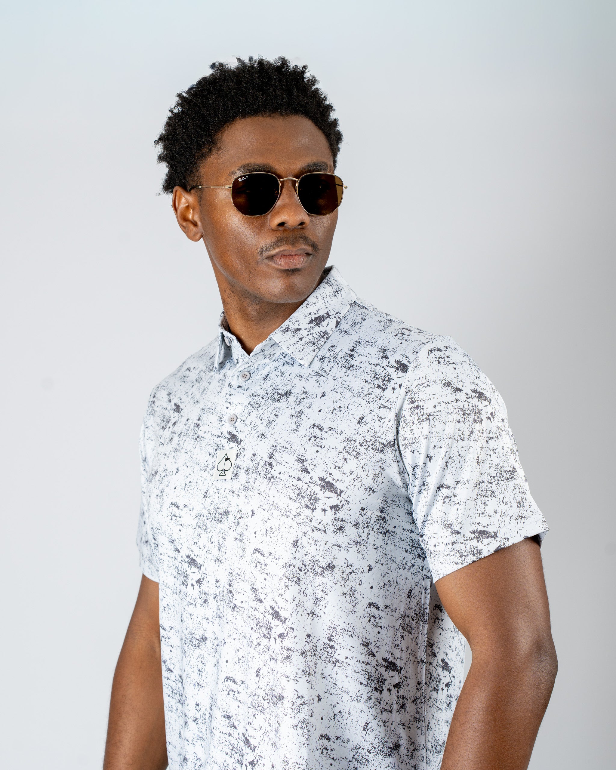 Model wearing a stylish white and black patterned golf shirt, paired with sunglasses, showcasing bold golf fashion.