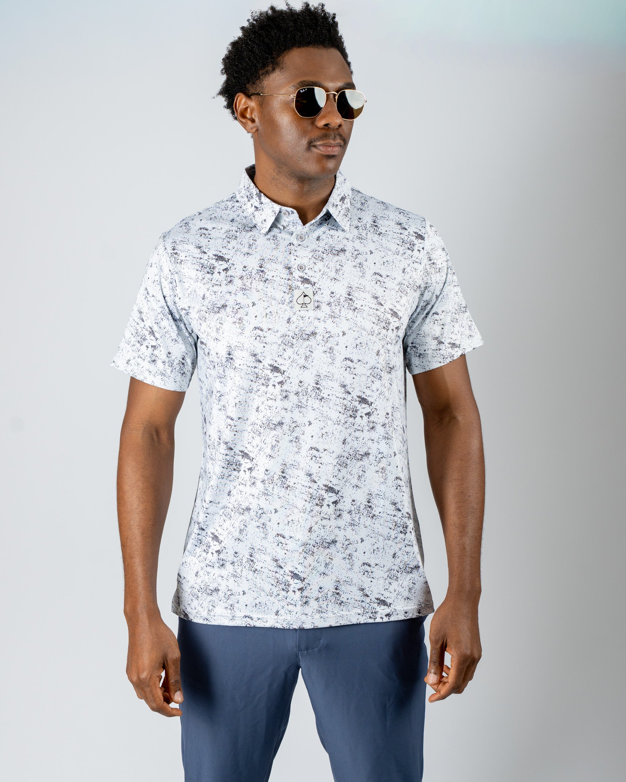 Stylish golfer wearing a white noise patterned polo shirt, paired with sunglasses and navy golf pants, showcasing bold golf fashion.