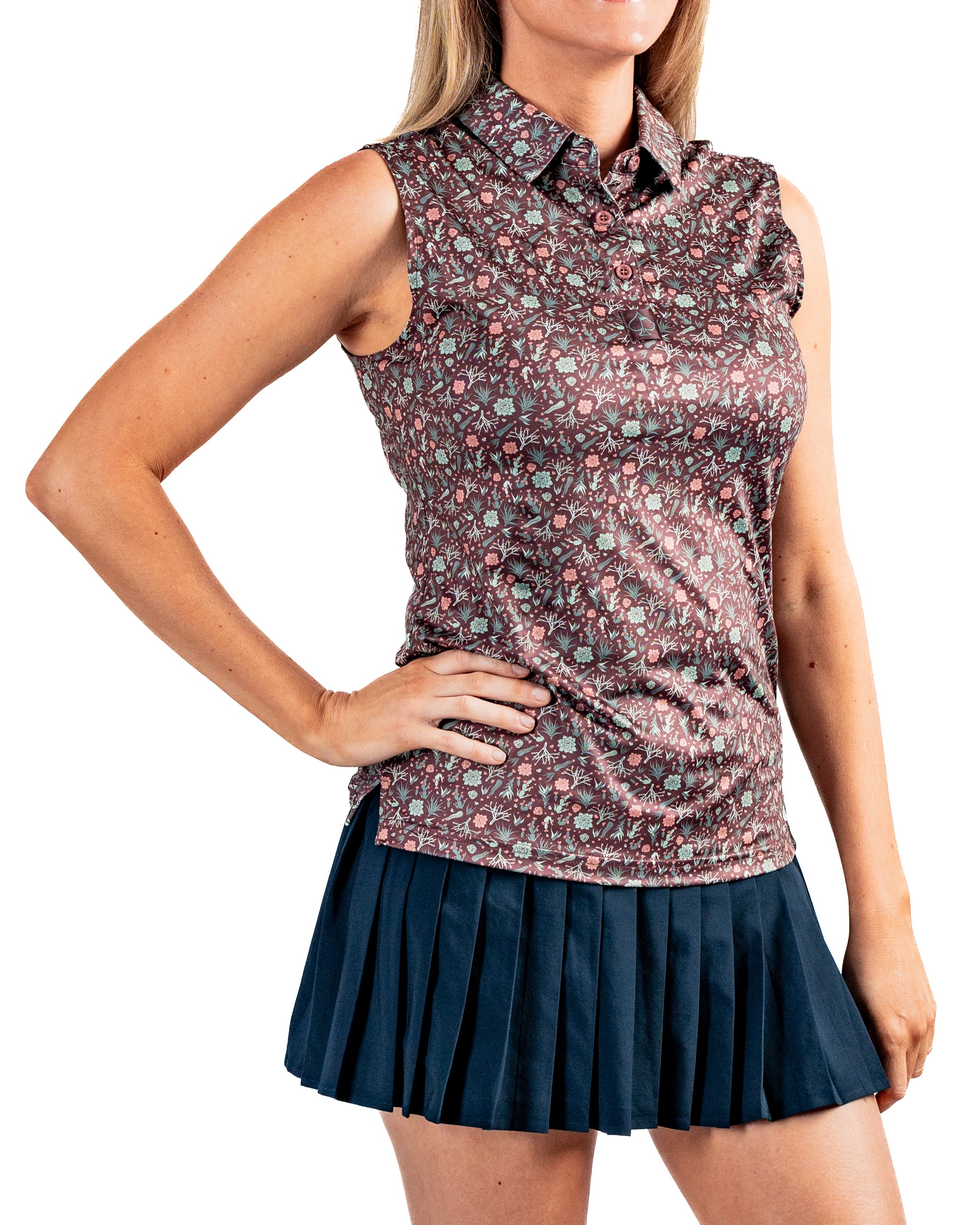 Women's Desert Sage sleeveless golf shirt featuring a floral pattern, paired with a pleated navy golf skirt.