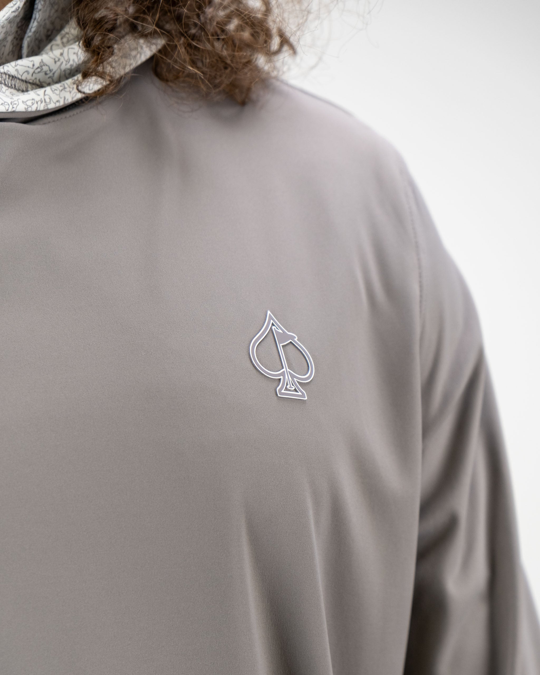 Men's performance golf hoodie in a neutral tone featuring a subtle spade logo, designed for comfort and style on the course.