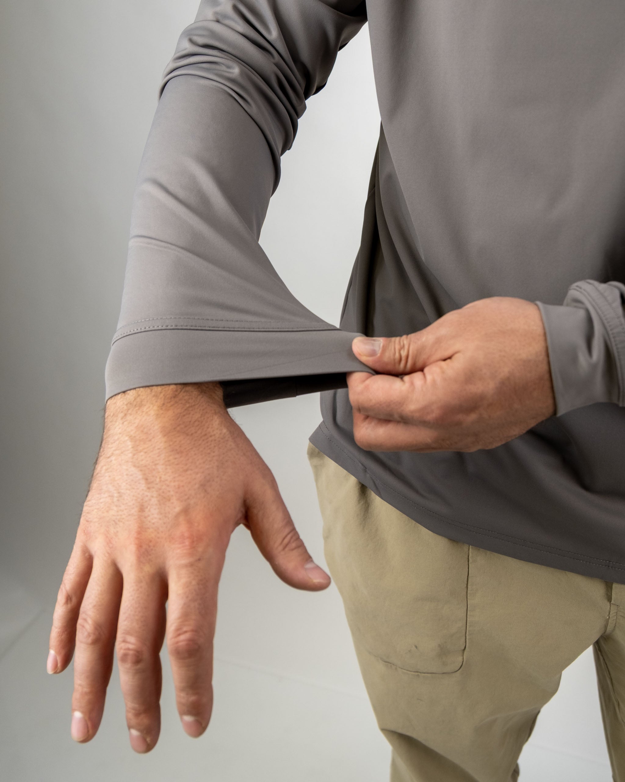 Man adjusting the sleeve of a Performance Golf Hoodie in a neutral color, showcasing its comfortable fit and flexibility.