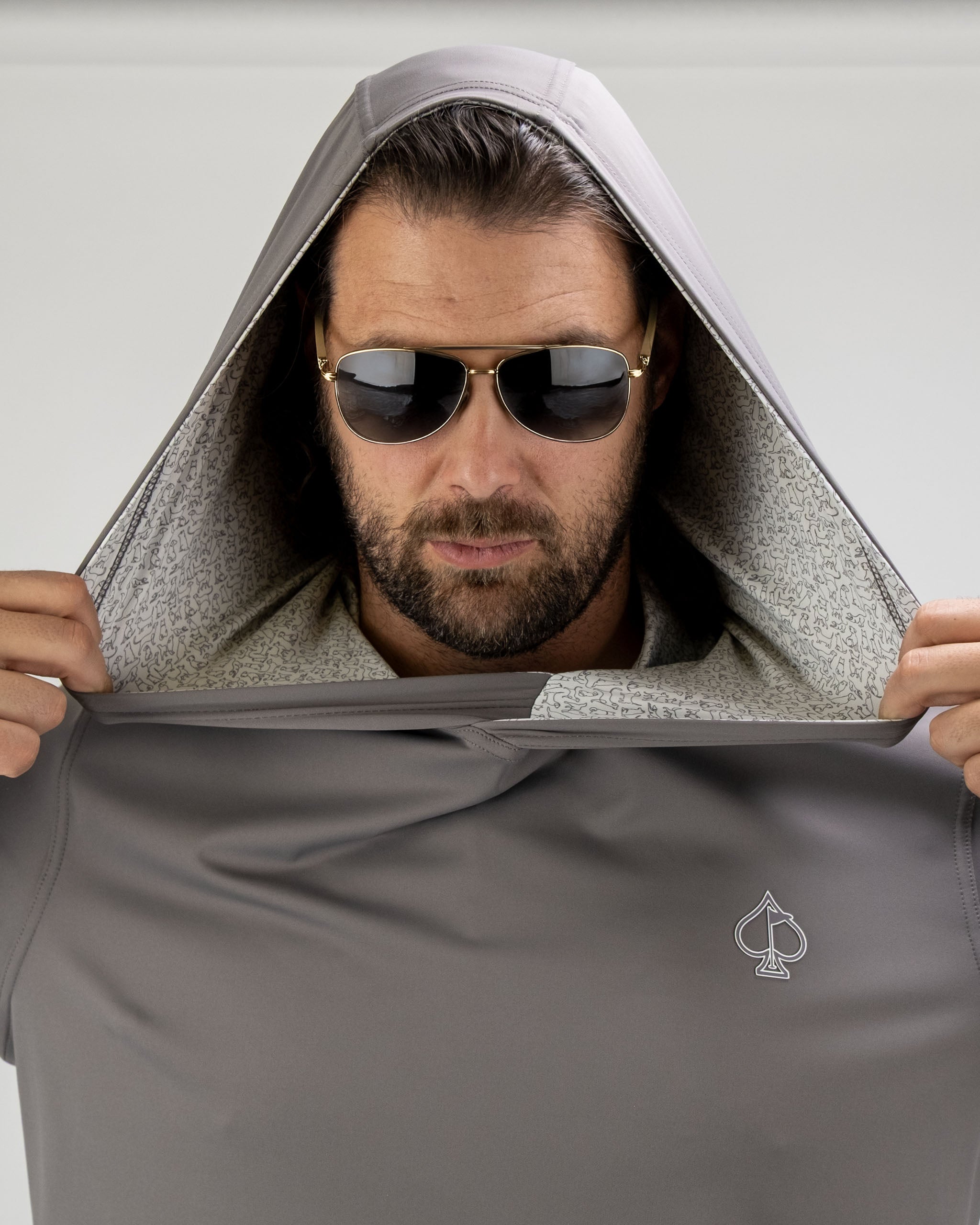 Man wearing a gray performance golf hoodie with a hood up, showcasing the interior pattern and sunglasses.