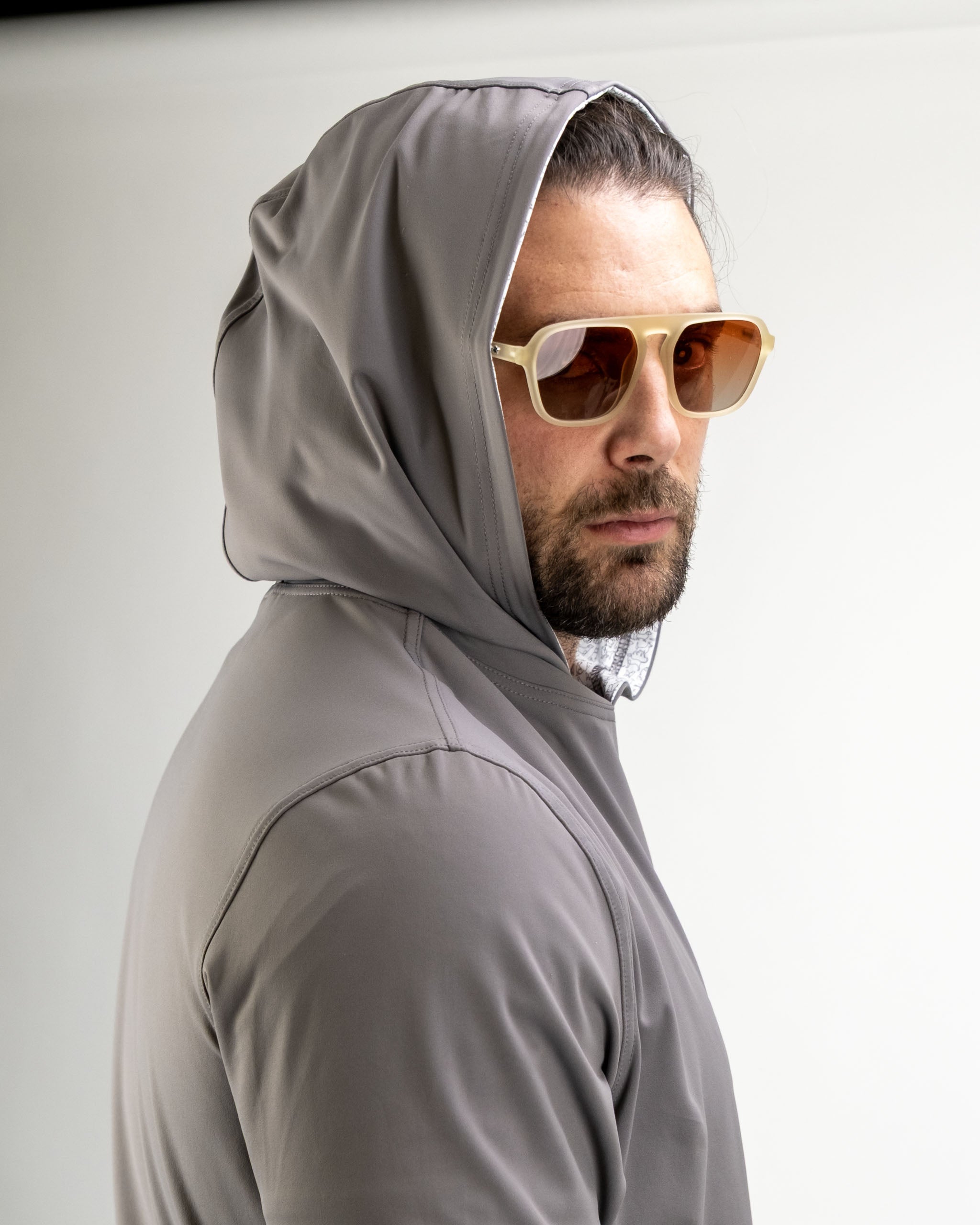 Man wearing a gray performance golf hoodie with a hood, looking confidently over his shoulder while wearing sunglasses.