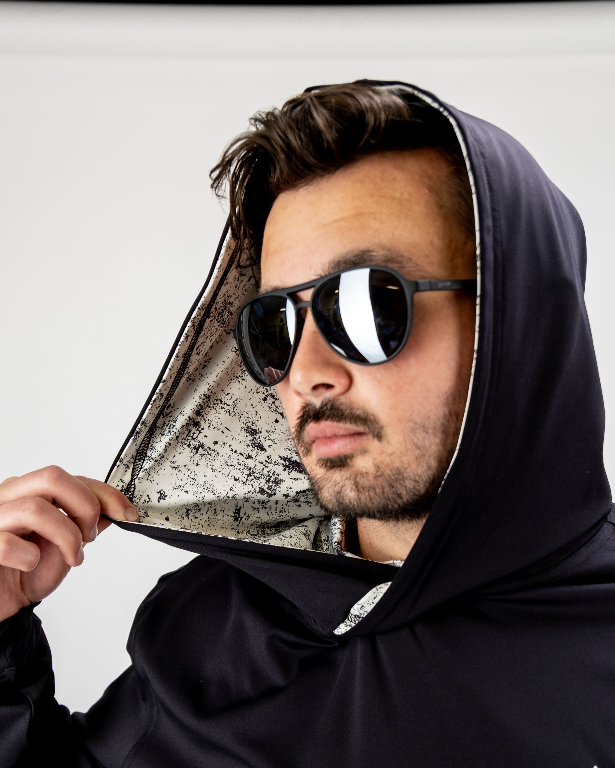 Man wearing a black performance golf hoodie with a unique patterned lining, adjusting the hood while wearing sunglasses.