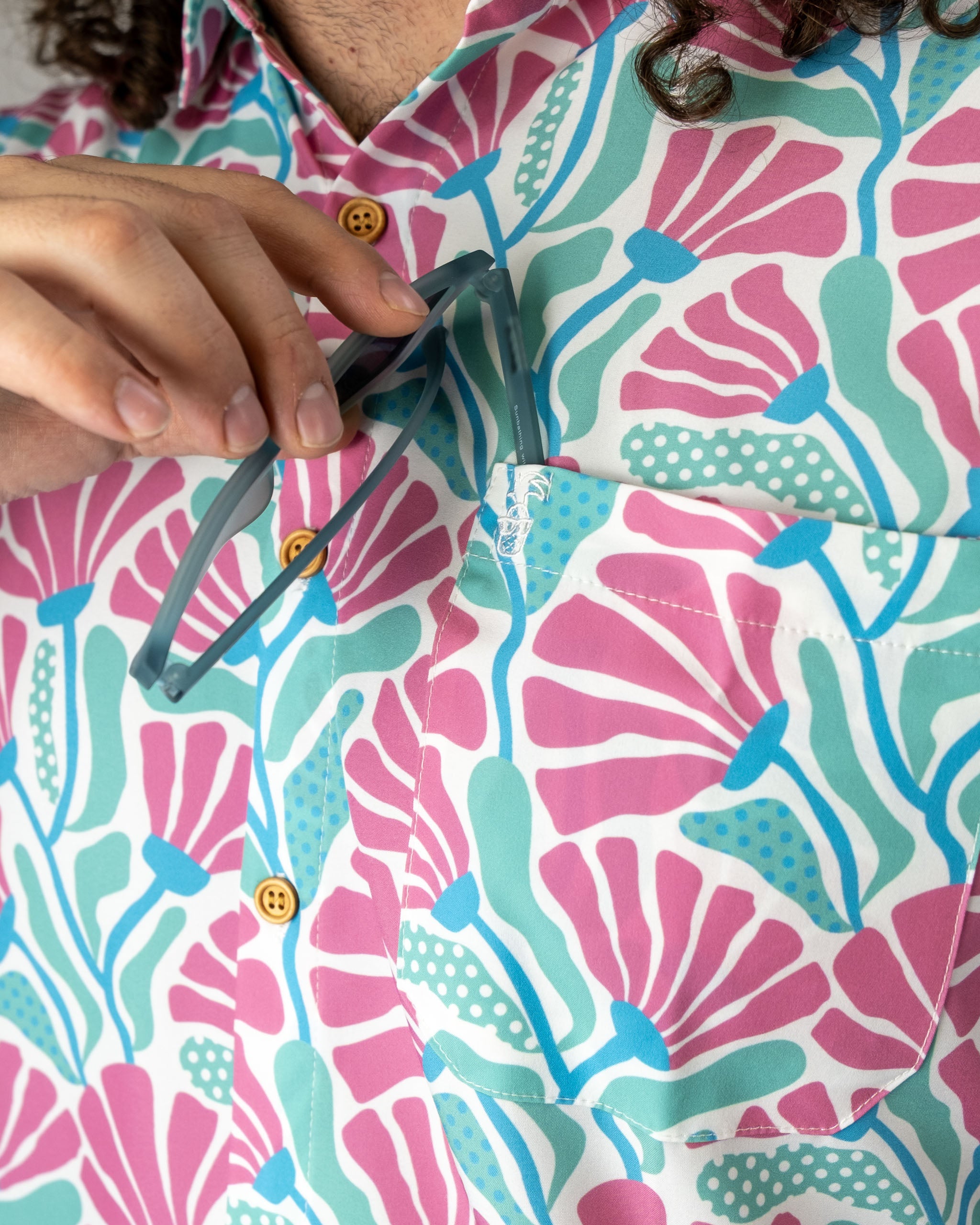 Colorful short-sleeve shirt featuring a coral and teal floral pattern, with a pocket holding sunglasses.