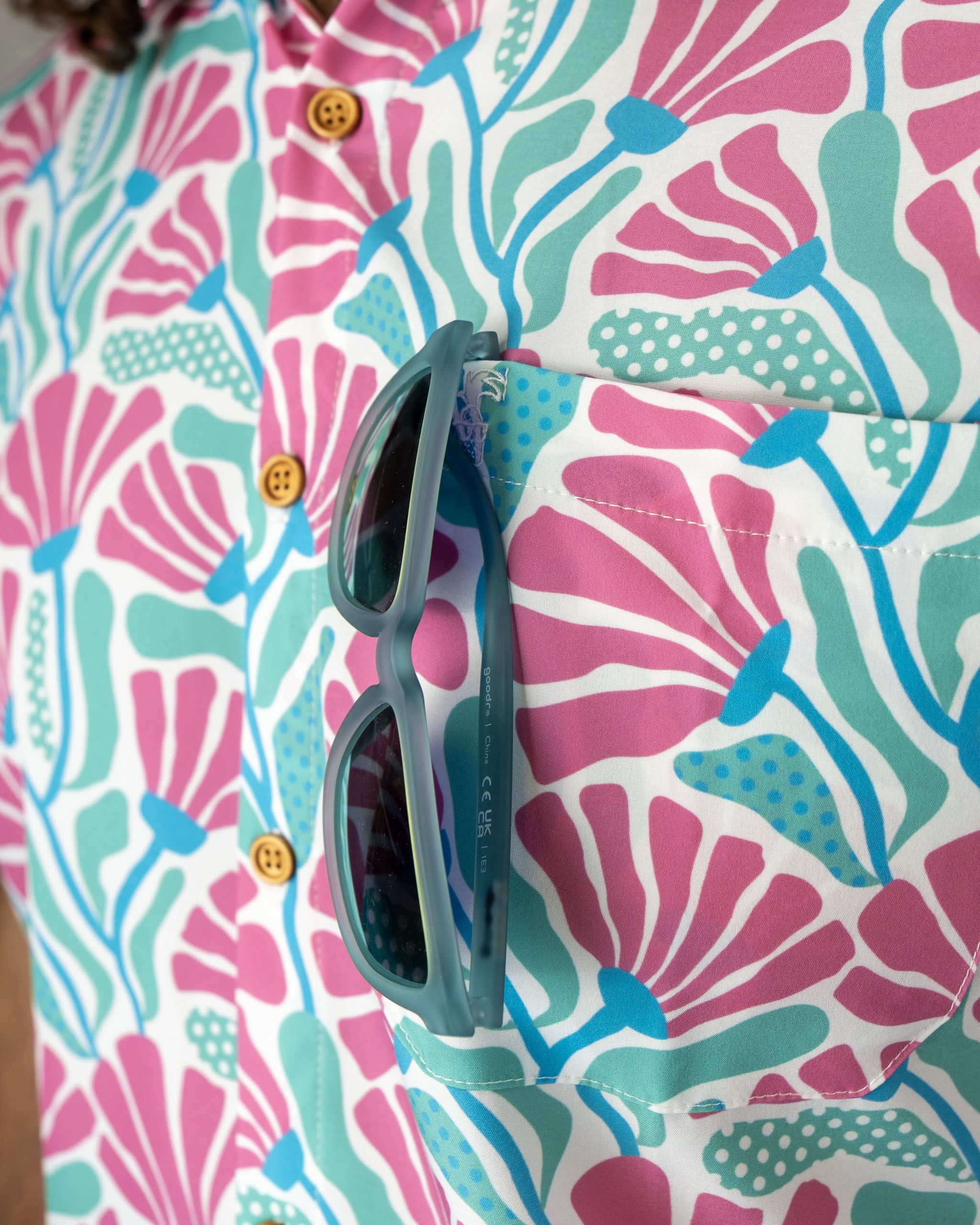 Colorful coral-patterned shirt featuring shades of pink and blue, with sunglasses resting in the chest pocket.