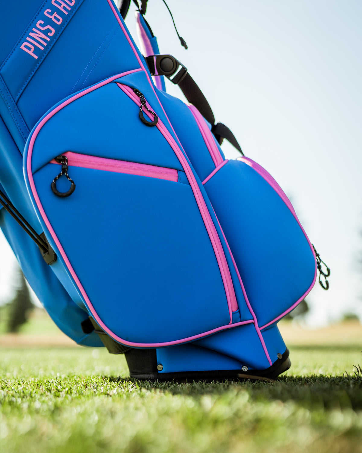 Vibrant blue raspberry golf bag with pink accents, featuring multiple pockets for storage on a golf course.