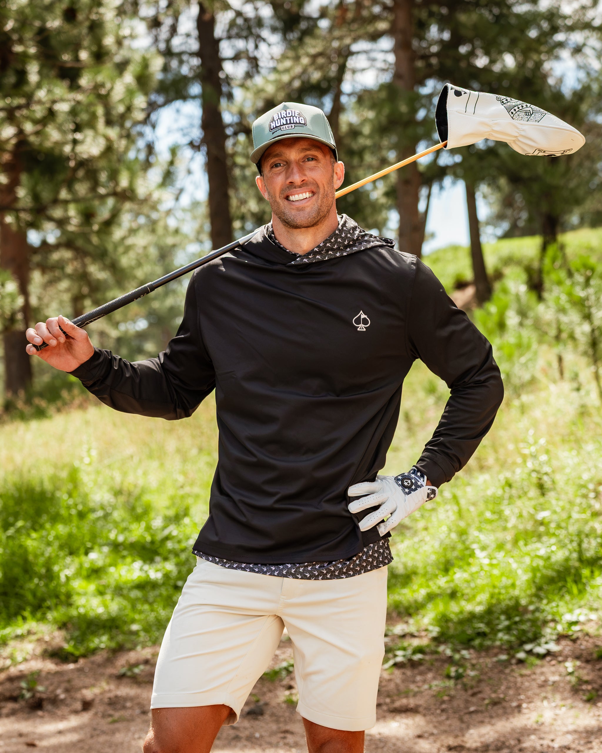 Performance golf hoodie in black with a duck hook design, worn by a smiling golfer holding a club in a natural setting.