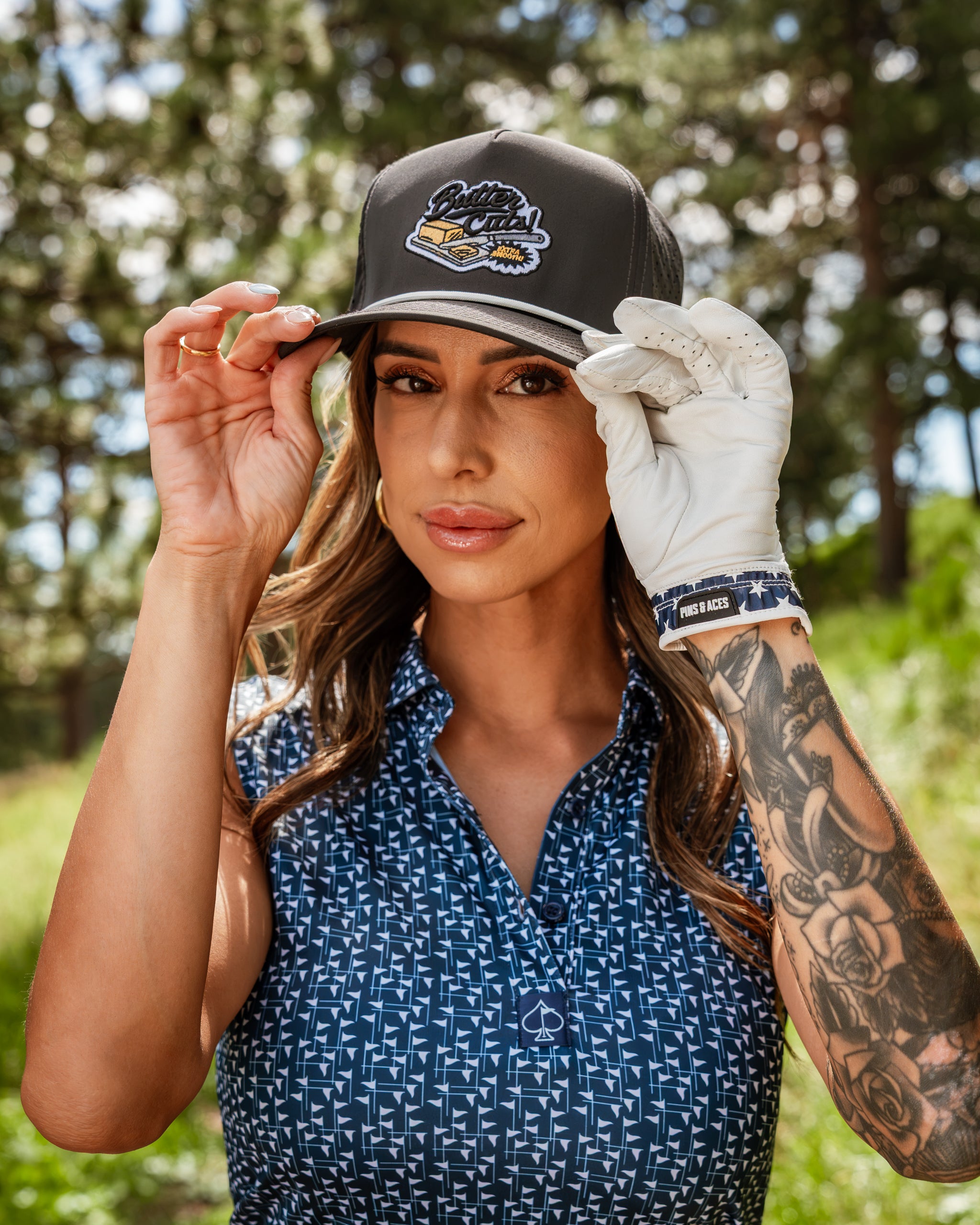 Navy and white women's golf shirt paired with a stylish cap, showcasing a bold logo and a golf glove, set outdoors.