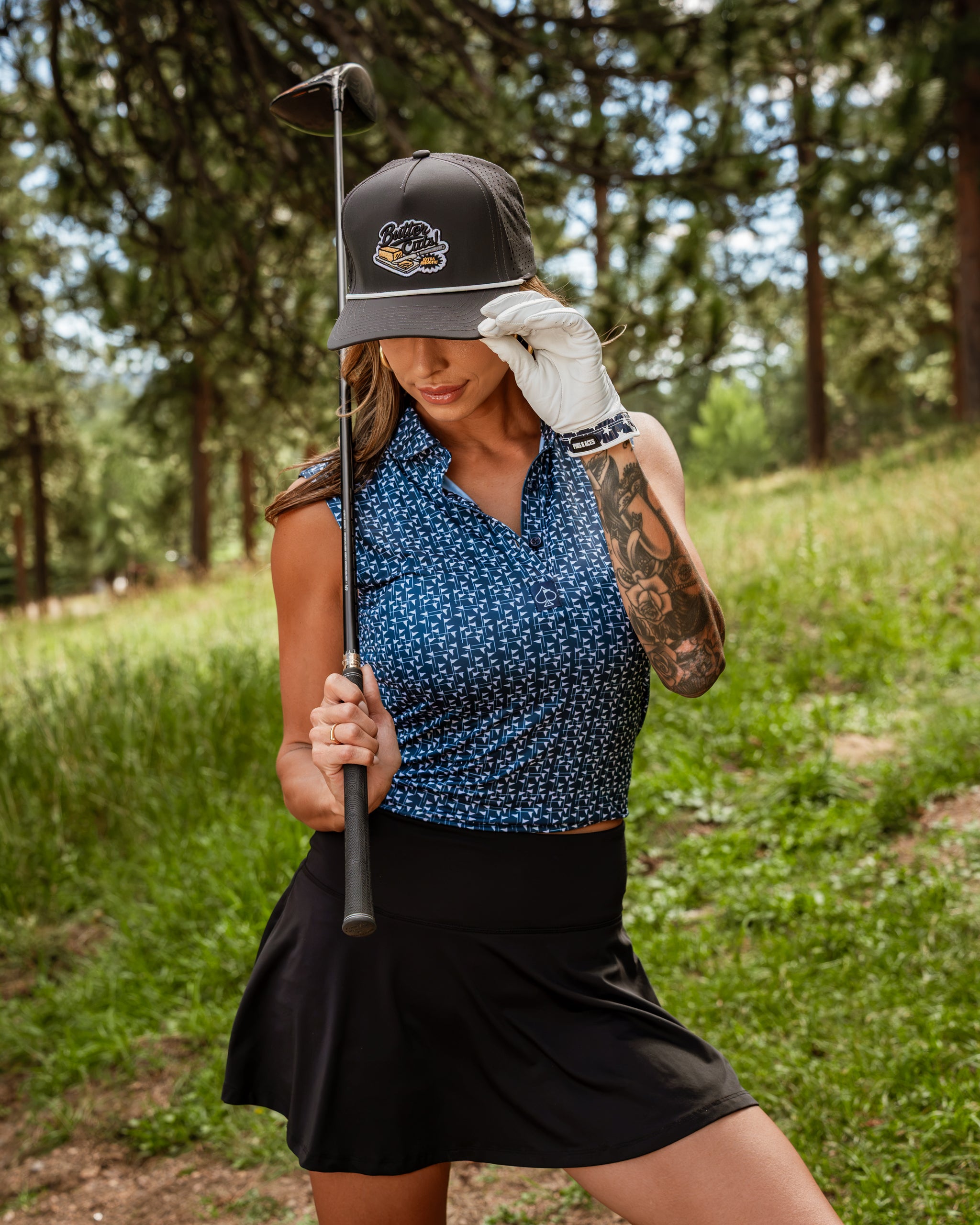 Navy and white women's golf polo with a stylish design, paired with a black skirt and golf accessories on a sunny course.