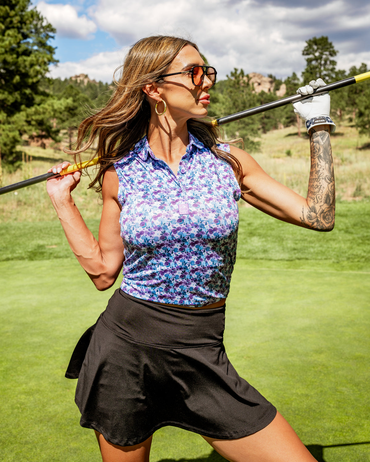 Stylish woman in a floral golf top and black skirt poses confidently on the course, showcasing women's white golf pedals.