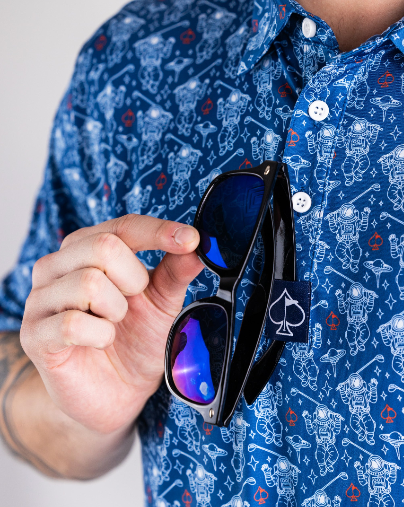 A person holding sunglasses in front of a blue patterned shirt featuring NASA space walkers and designs.