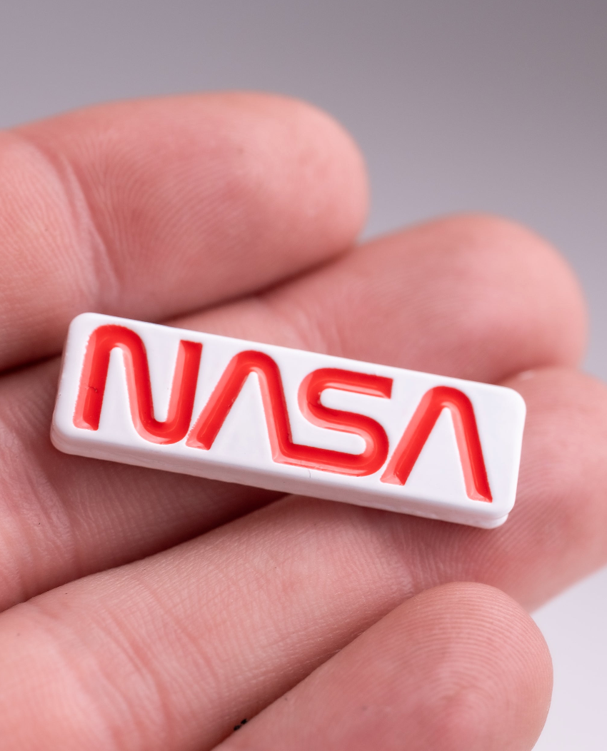 NASA "Worm" ball marker in a hand, featuring a bold red logo on a white background, perfect for golf enthusiasts.
