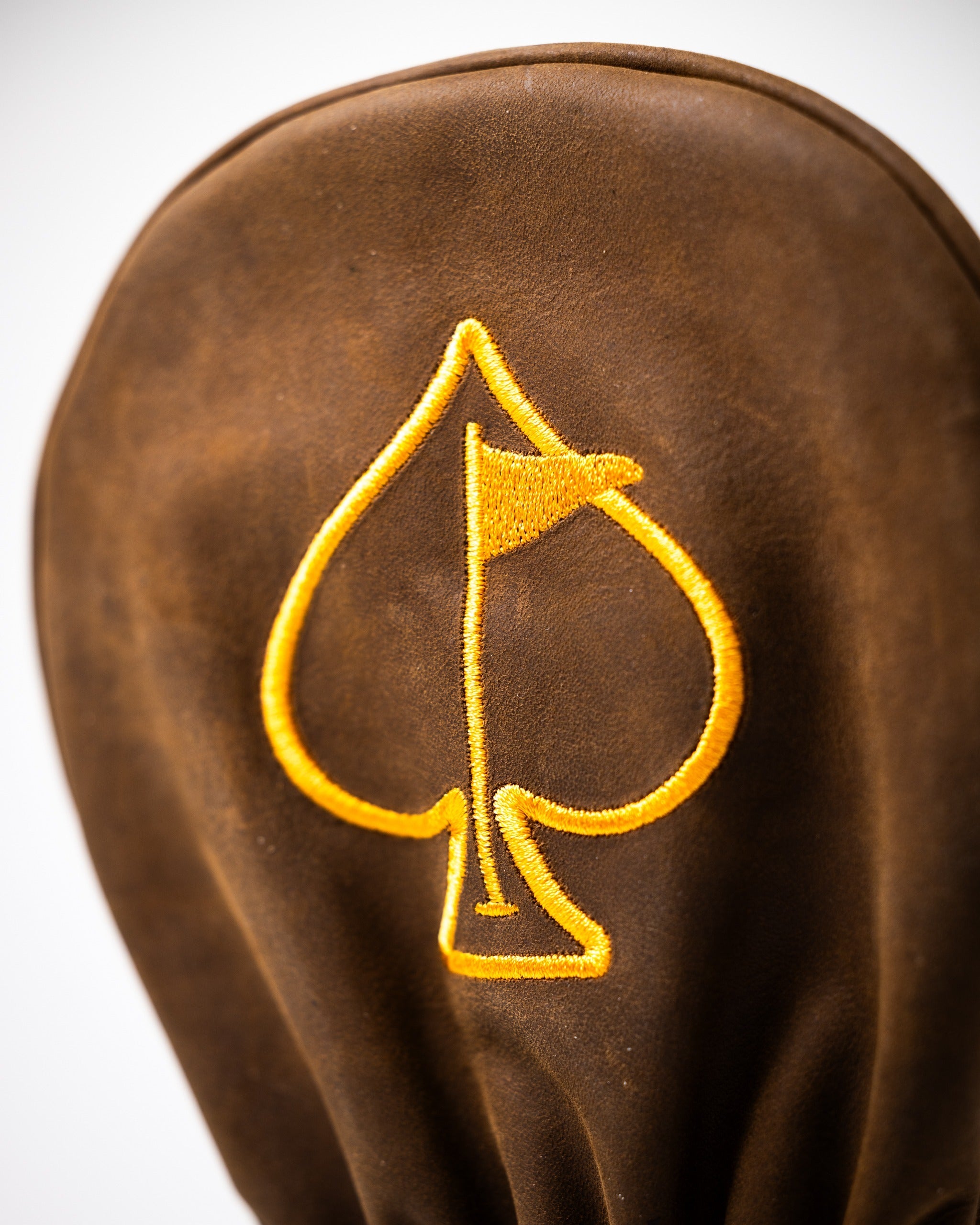 Brown leather driver cover featuring a bold yellow spade emblem, perfect for golfers seeking a stylish accessory.