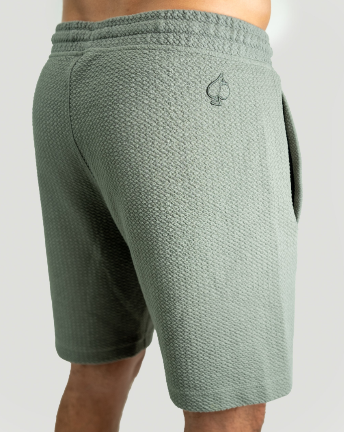 Waffleknit shorts in sage green featuring a textured fabric and a subtle logo on the back pocket. Ideal for casual comfort.