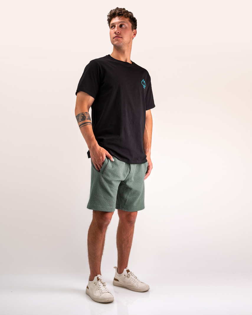 Stylish man wearing black t-shirt and sage green waffleknit shorts, showcasing a casual golf-ready look.