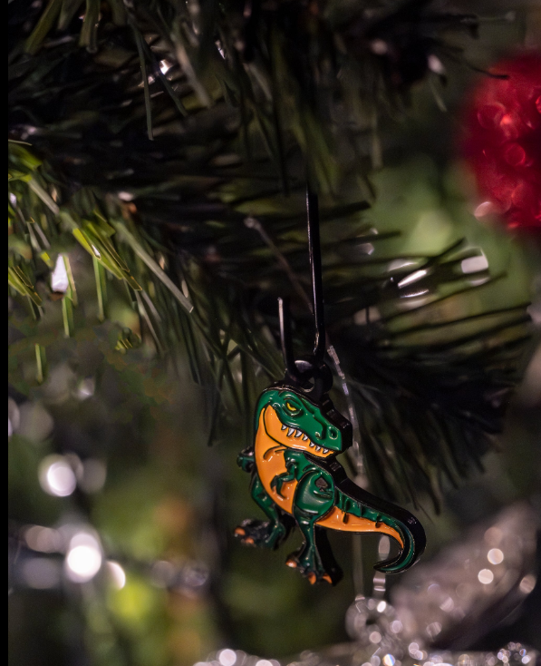 Colorful T-Rex ornament hanging on a Christmas tree, featuring vibrant green and orange details against festive lights.