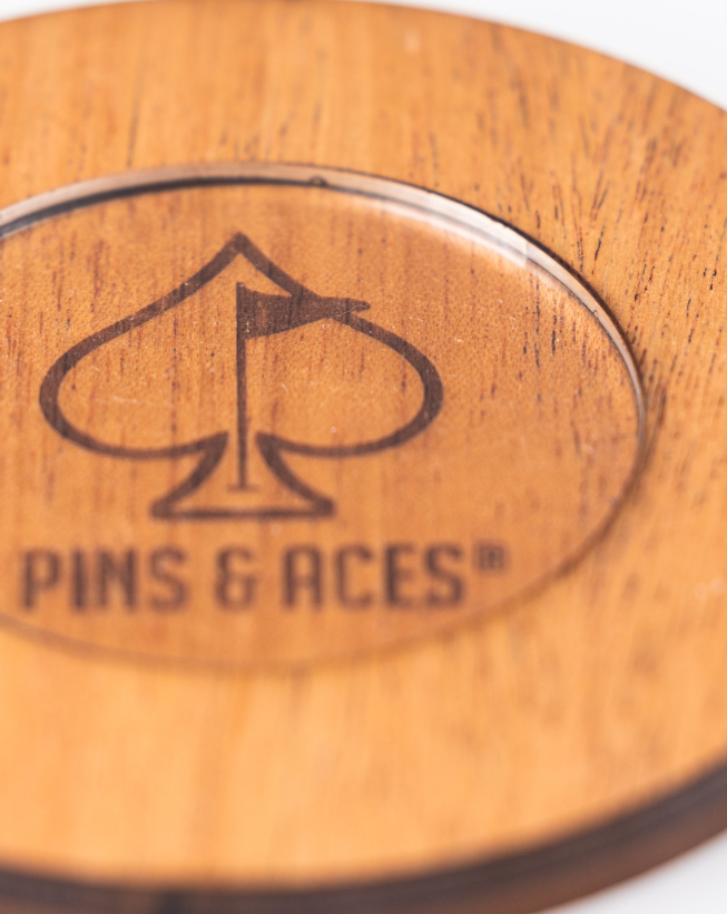 Wooden coaster featuring the Pins & Aces logo, designed for golfers who appreciate stylish accessories on and off the course.