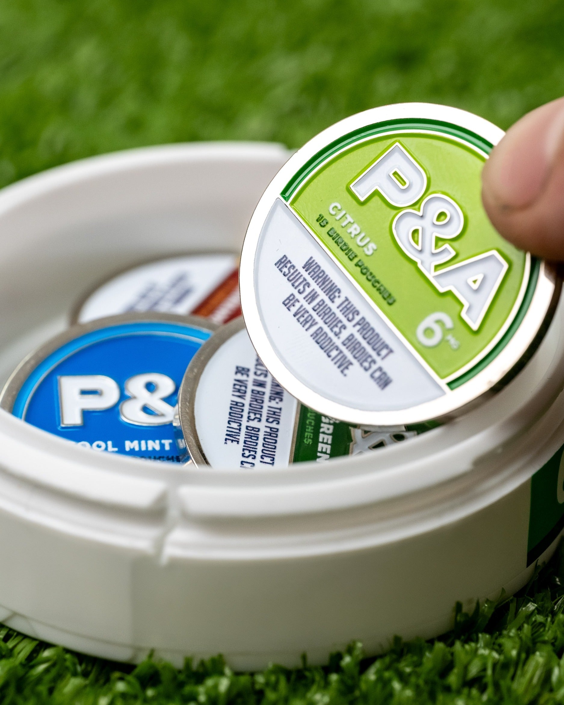 Citrus ball marker from Pins and Aces, featuring a vibrant design, stored in a round container with other markers.