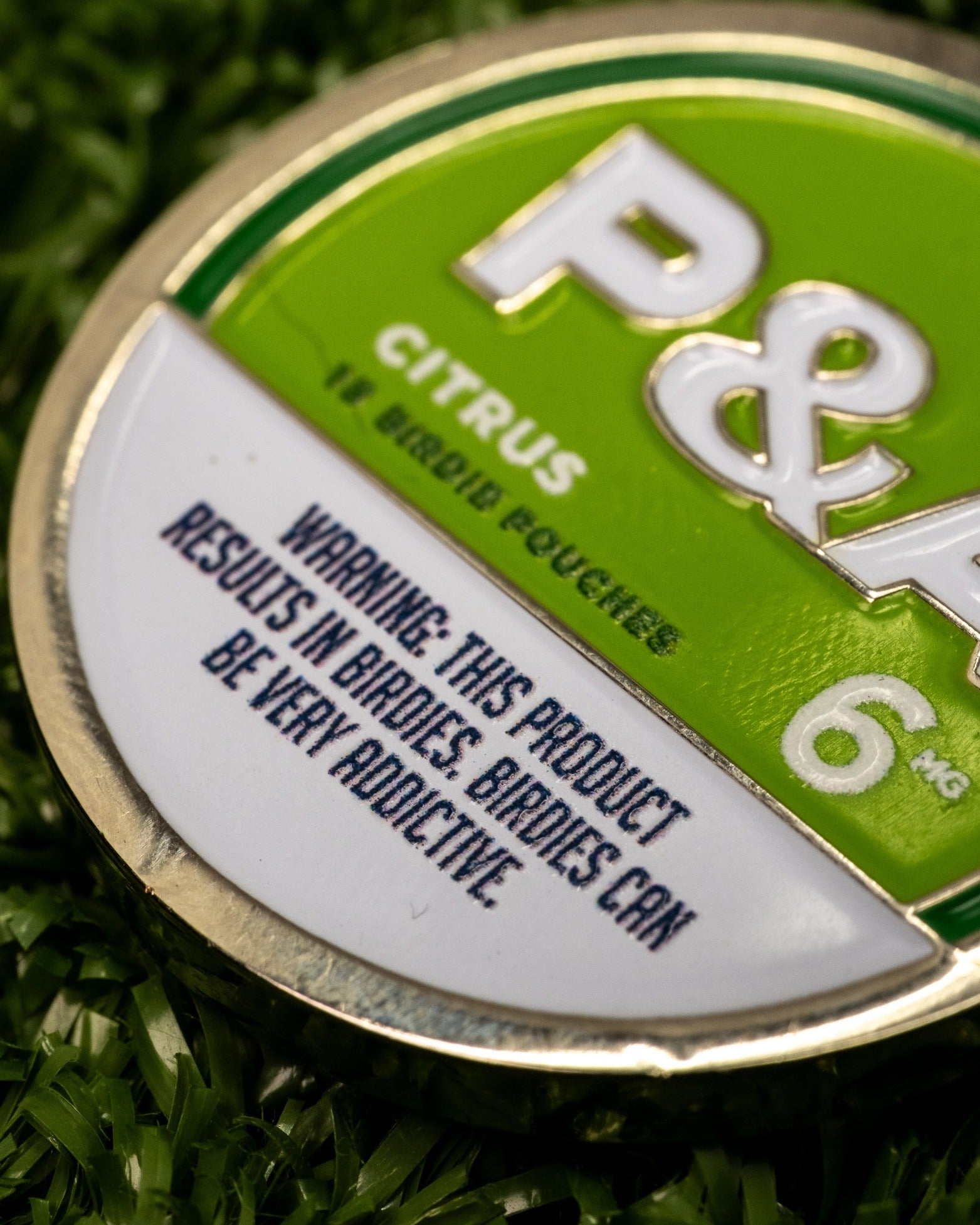 Citrus ball marker featuring a bold design with a warning about its addictive nature for birdie enthusiasts.