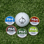 Citrus ball marker surrounded by four colorful markers on green turf, showcasing bold golf accessories for stylish play.