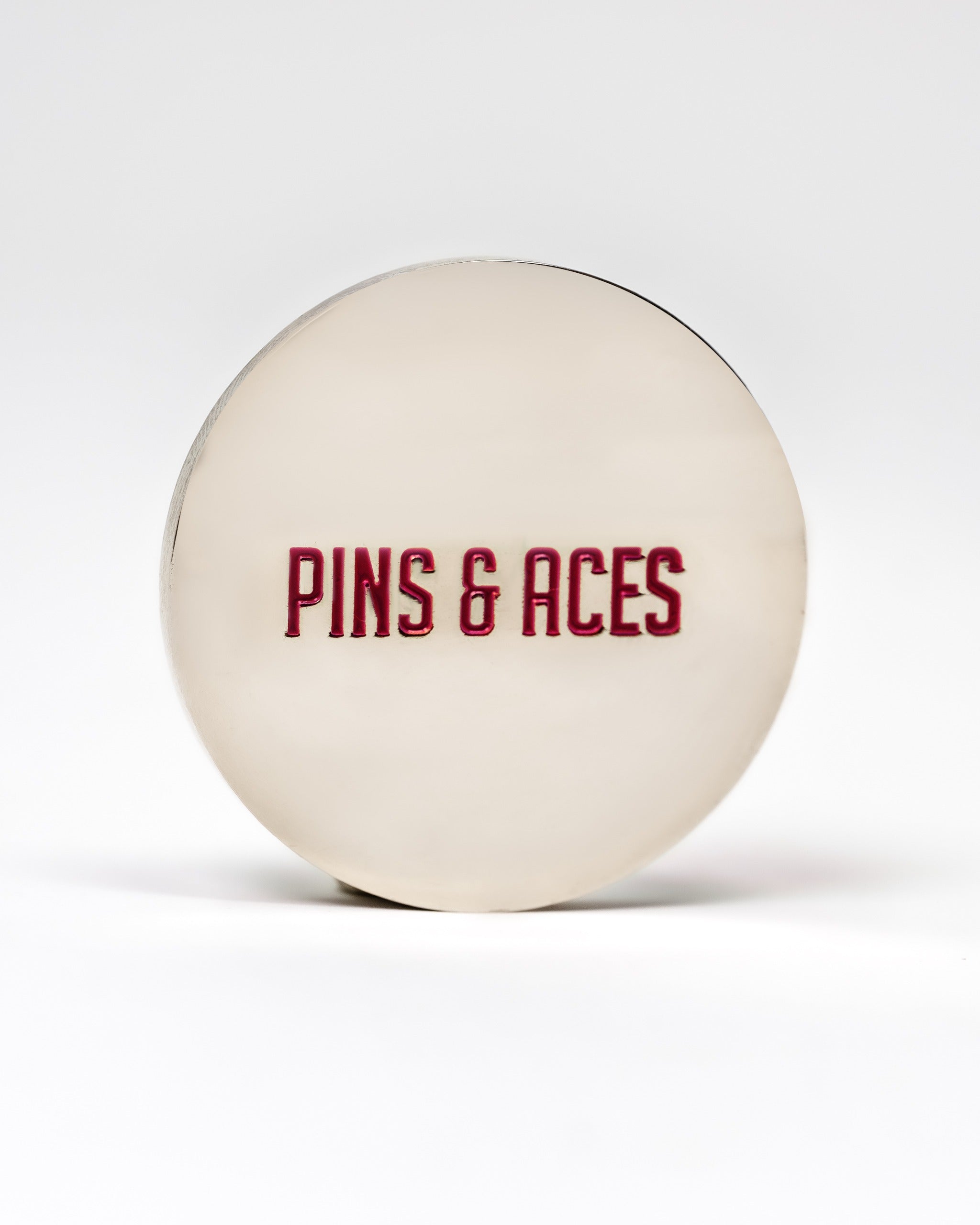 Smooth ball marker featuring a polished silver finish with "PINS & ACES" embossed in bold red letters.