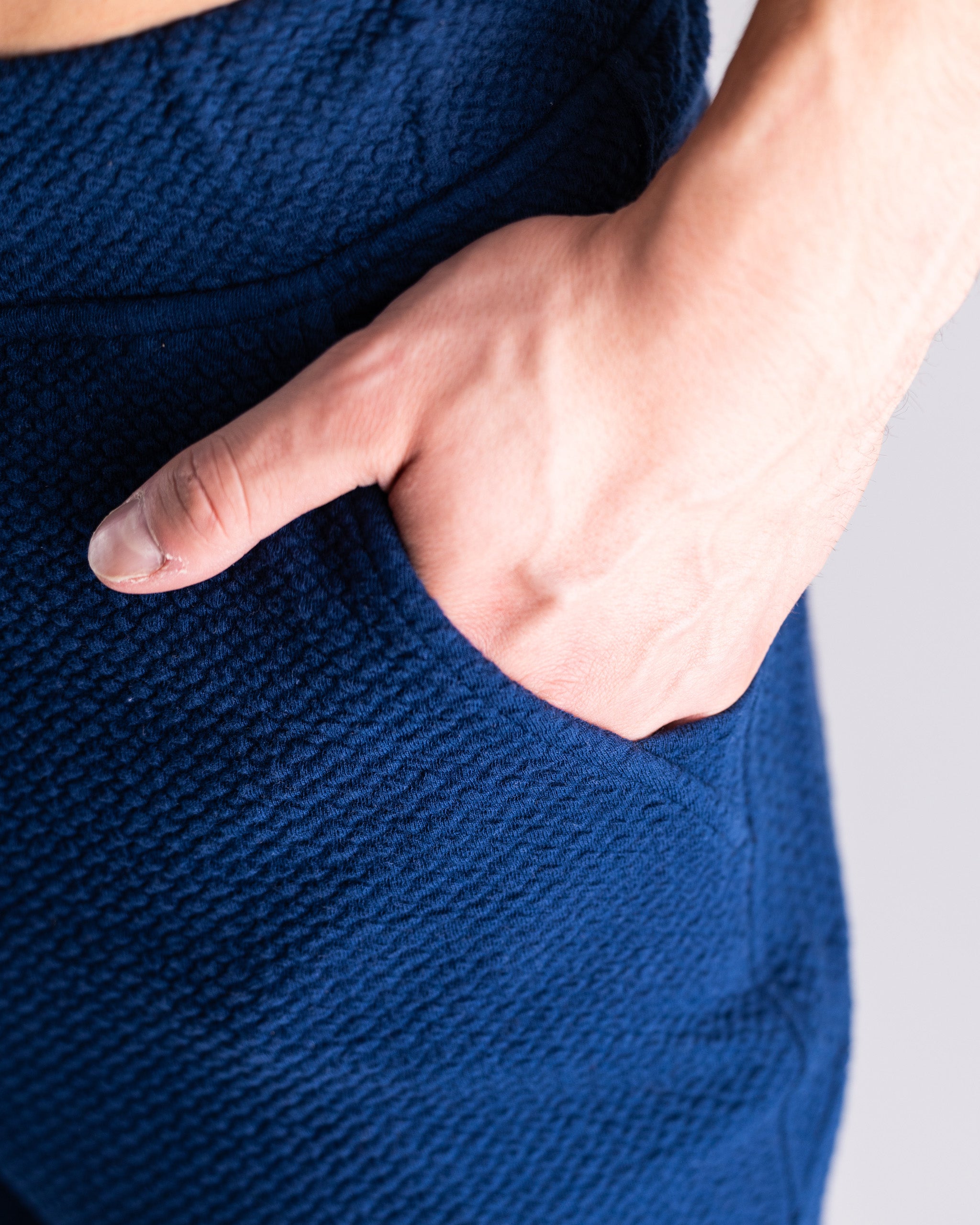 Close-up of a hand resting in the pocket of a navy waffle knit jogger, showcasing its textured fabric and relaxed fit.