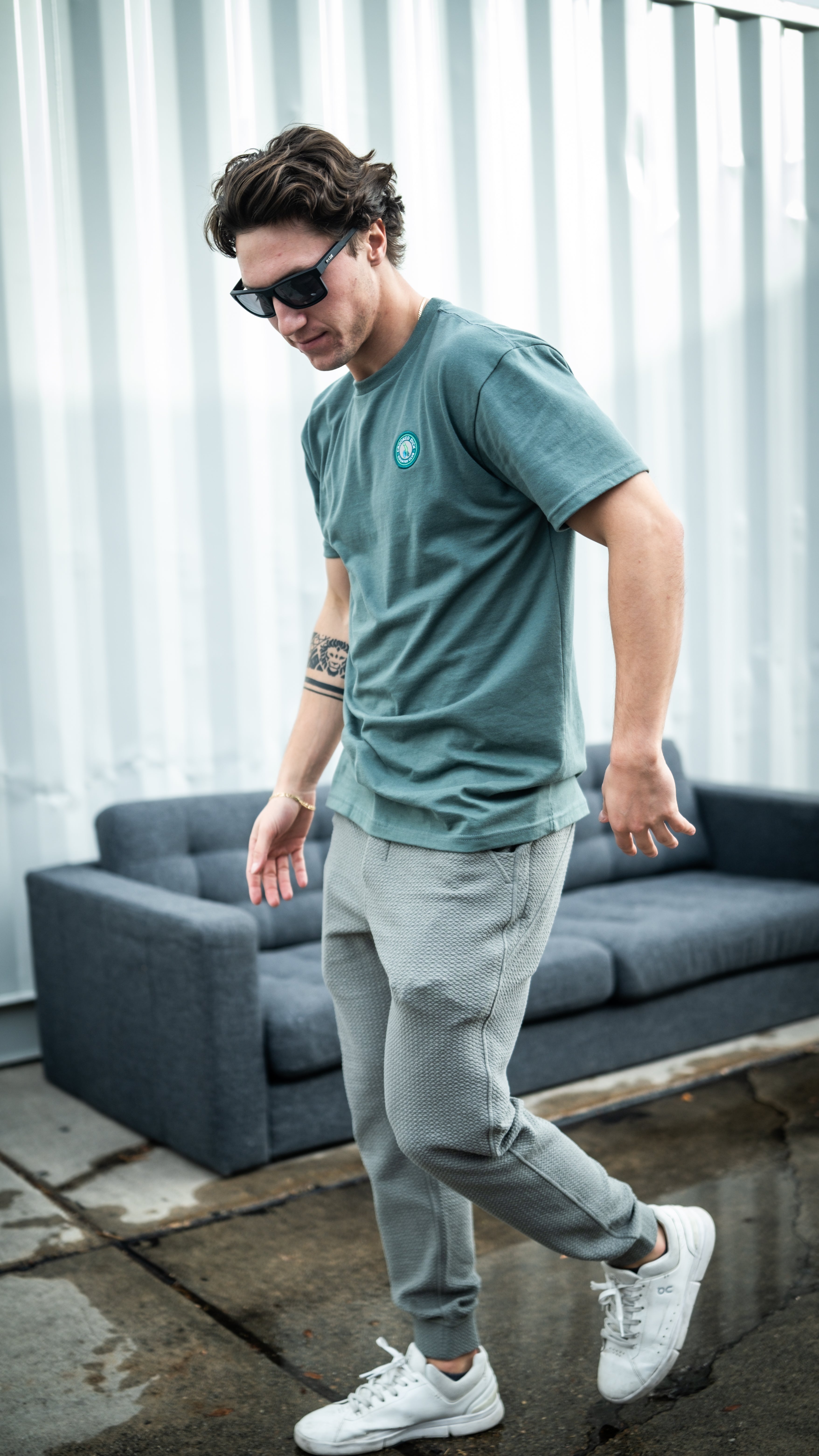 Man wearing sage green Player Preferred Waffleknit Jogger and matching t-shirt, walking on a wet surface near a couch.