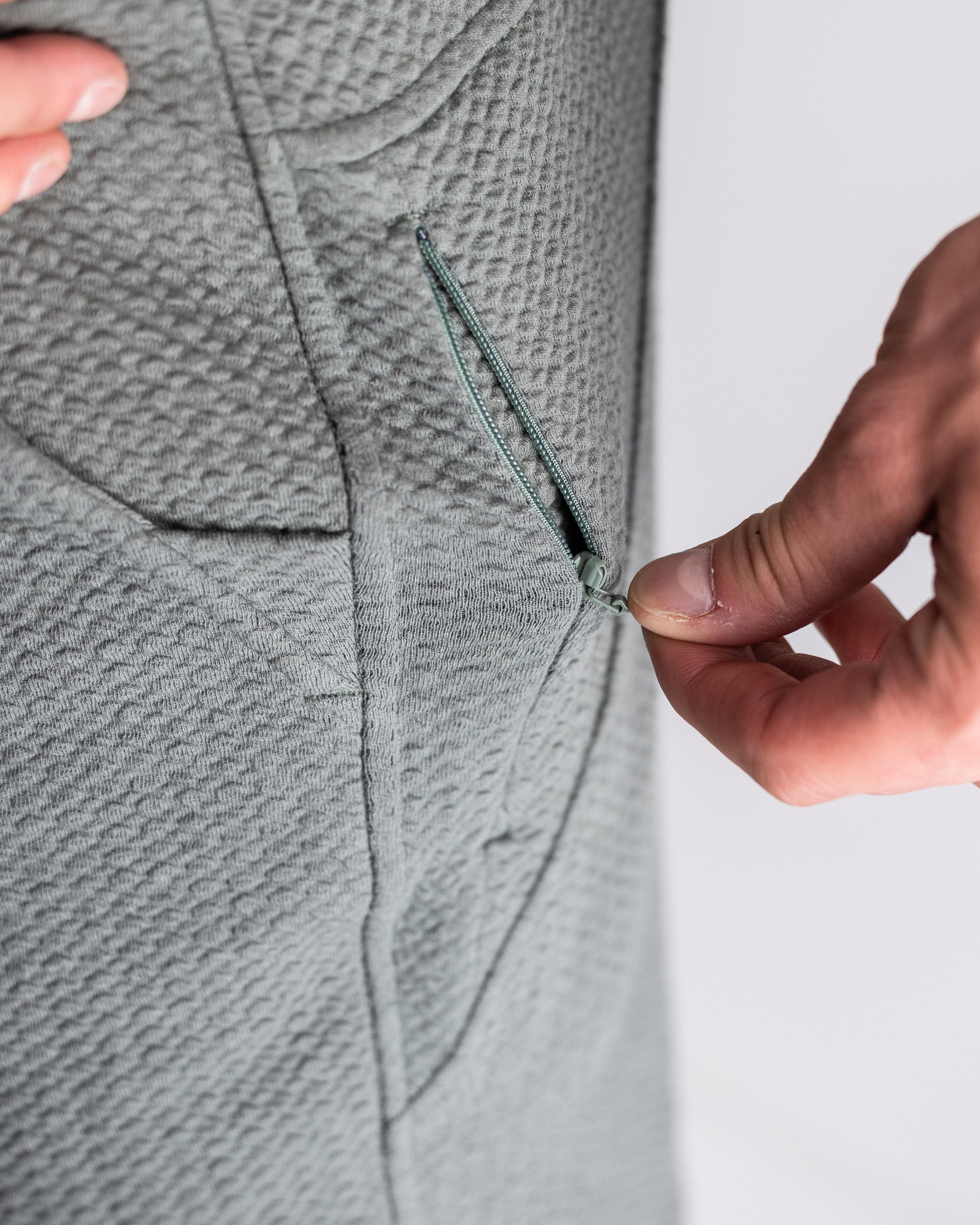 Close-up of a hand adjusting the zipper on the Player Preferred Waffleknit Jogger in sage green, showcasing its textured fabric.