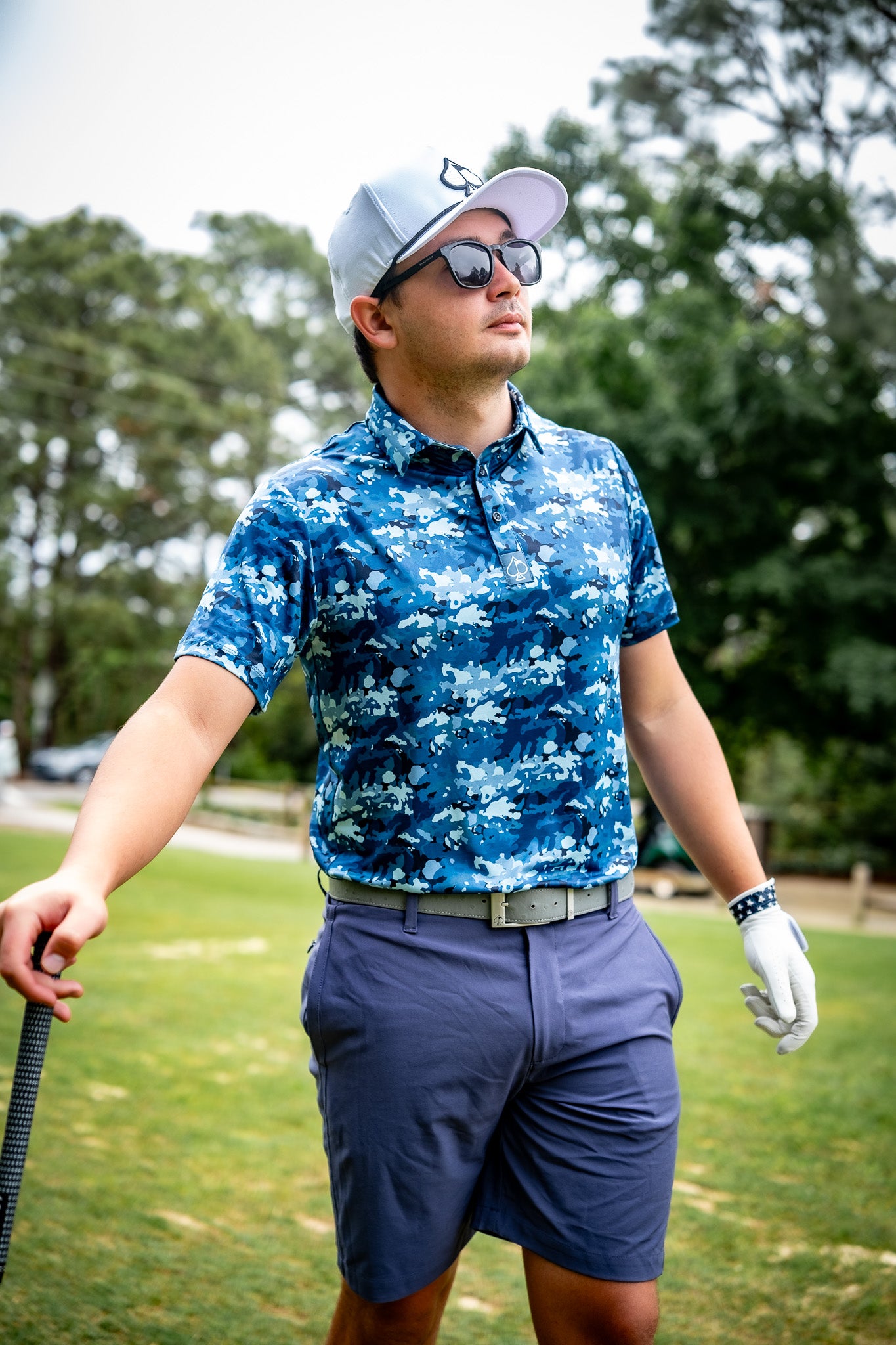 A golfer in stylish blue camo performance shorts and a matching shirt, standing confidently on the course.