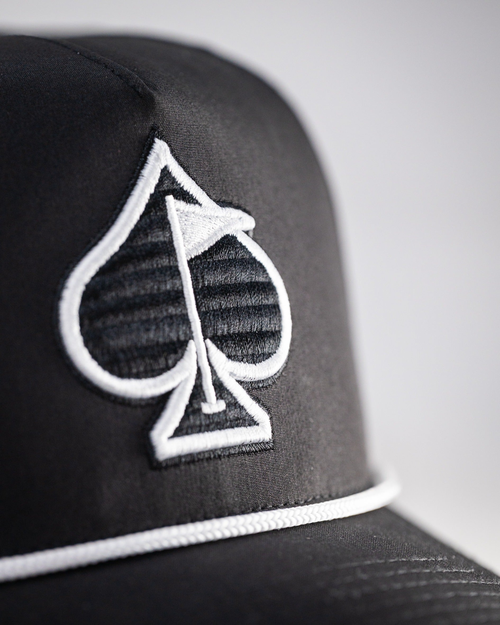 Black perforated rope hat featuring a stylish spade logo, perfect for golfers seeking a bold accessory on the course.