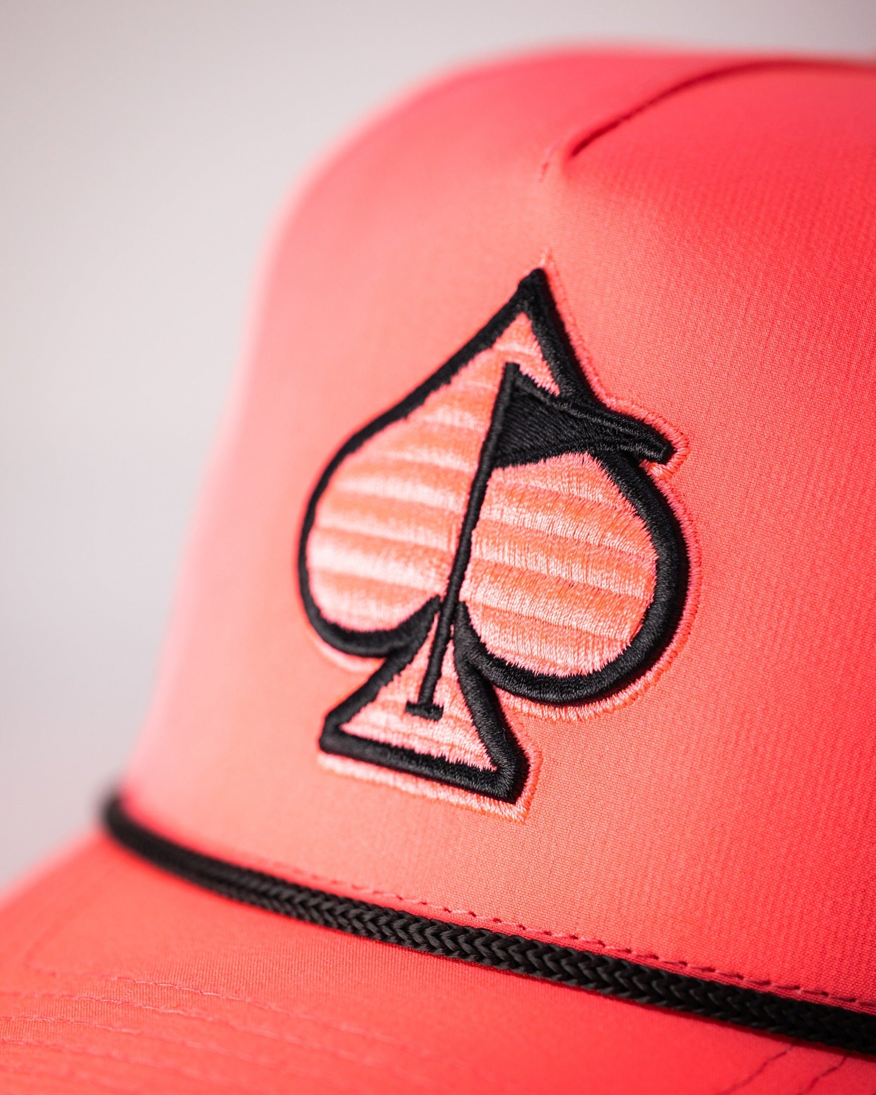 Highlighter pink perforated rope hat featuring a black spade logo, perfect for stylish golfers seeking standout accessories.