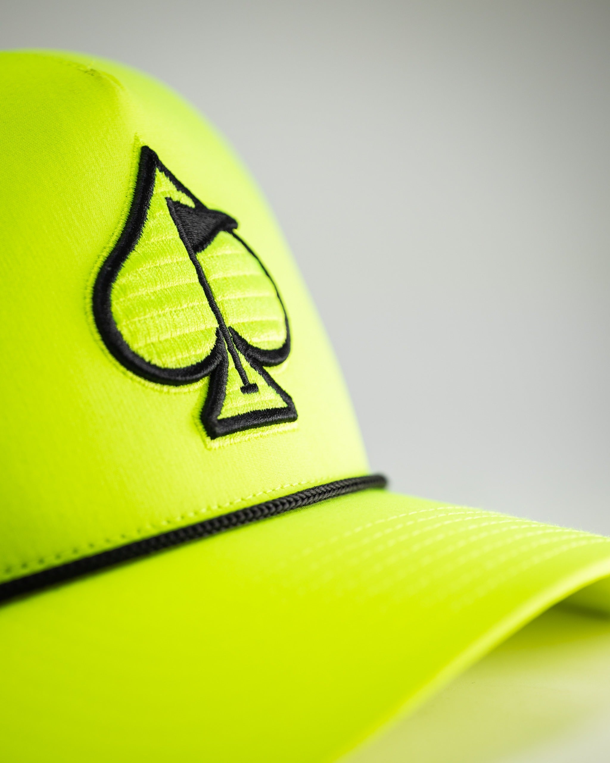 Highlighter yellow perforated rope hat featuring a black spade logo, perfect for bold golfers seeking style on the course.