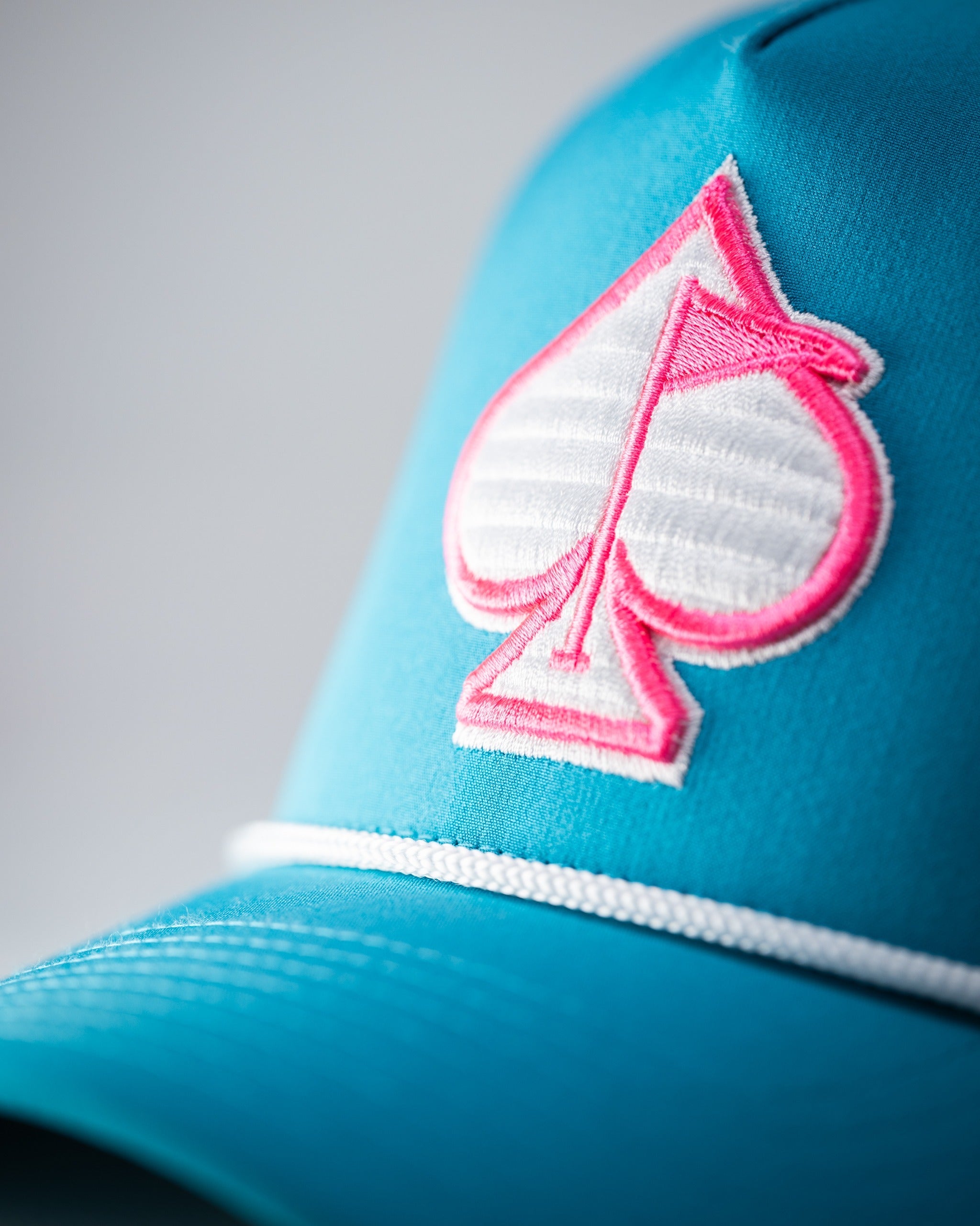 Perforated rope hat in baby blue featuring a pink spade logo, perfect for stylish golfers on the course.
