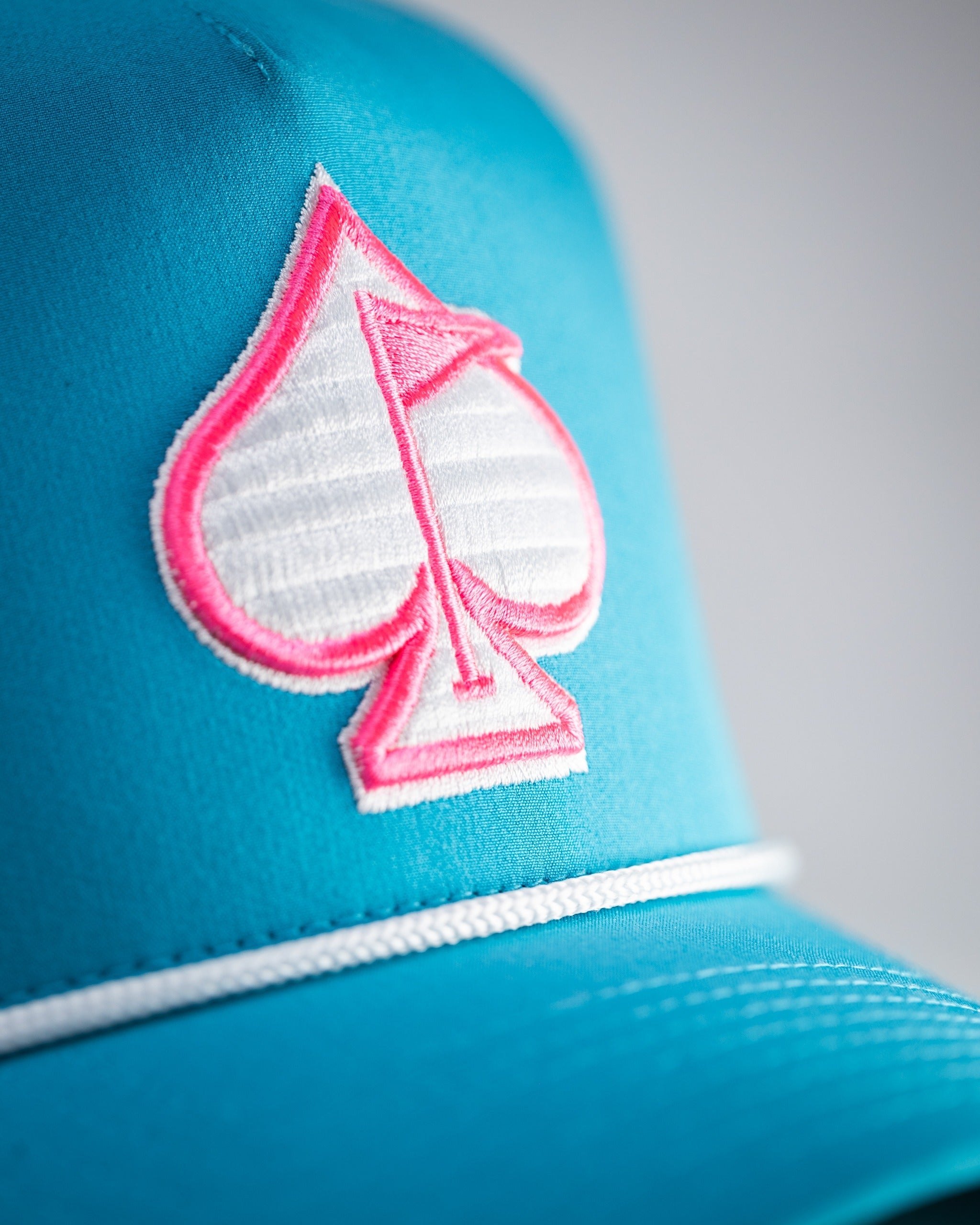 Perforated rope hat in baby blue featuring a pink spade logo, perfect for stylish golfers seeking standout accessories.