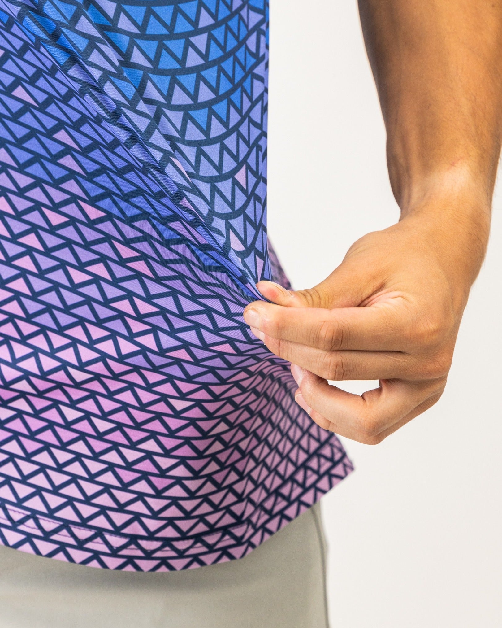 Close-up of a person holding the hem of a vibrant golf shirt featuring a digital rainfall pattern in blue and pink tones.