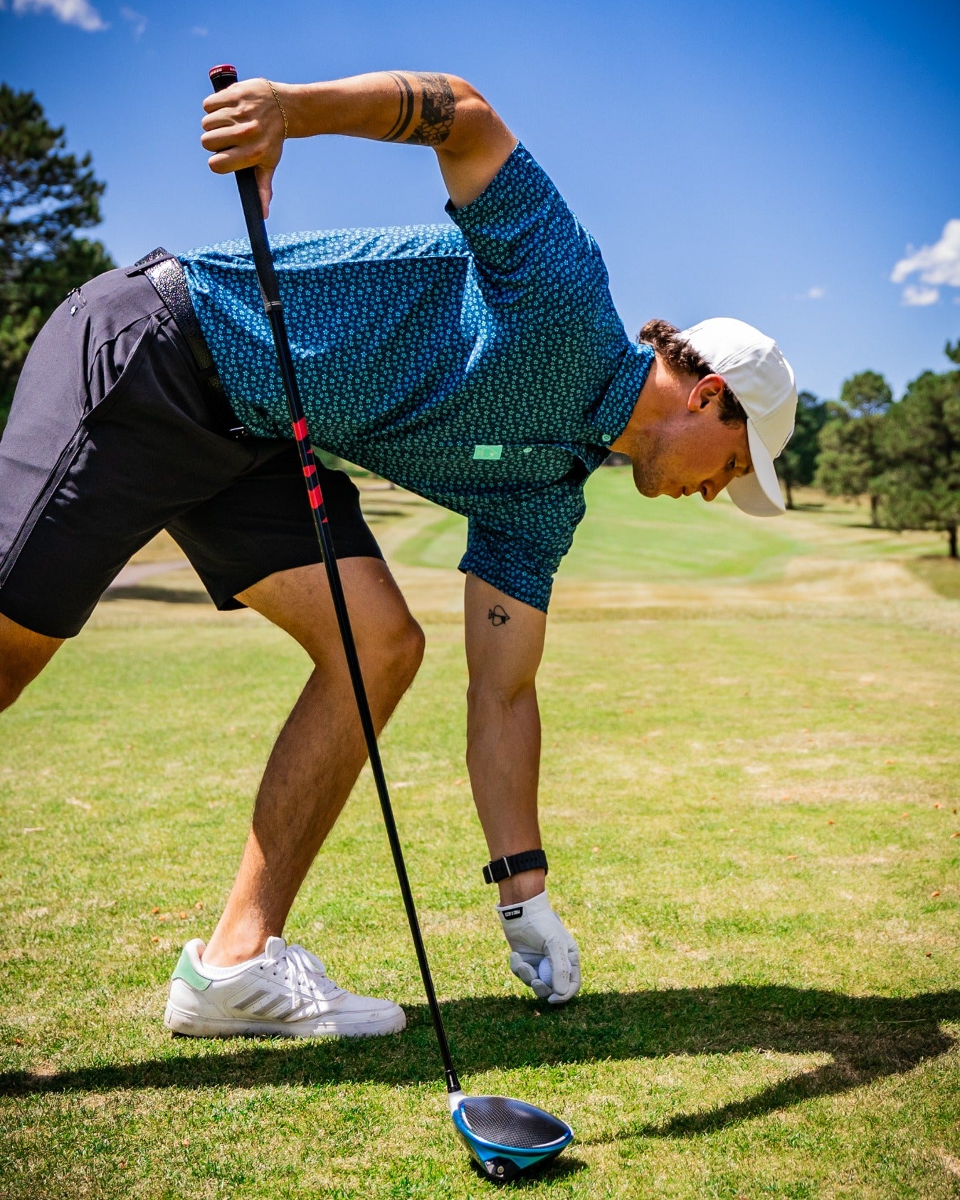 A golfer in a blue micro floral shirt prepares to tee off on a sunny course, showcasing bold golf style and confidence.