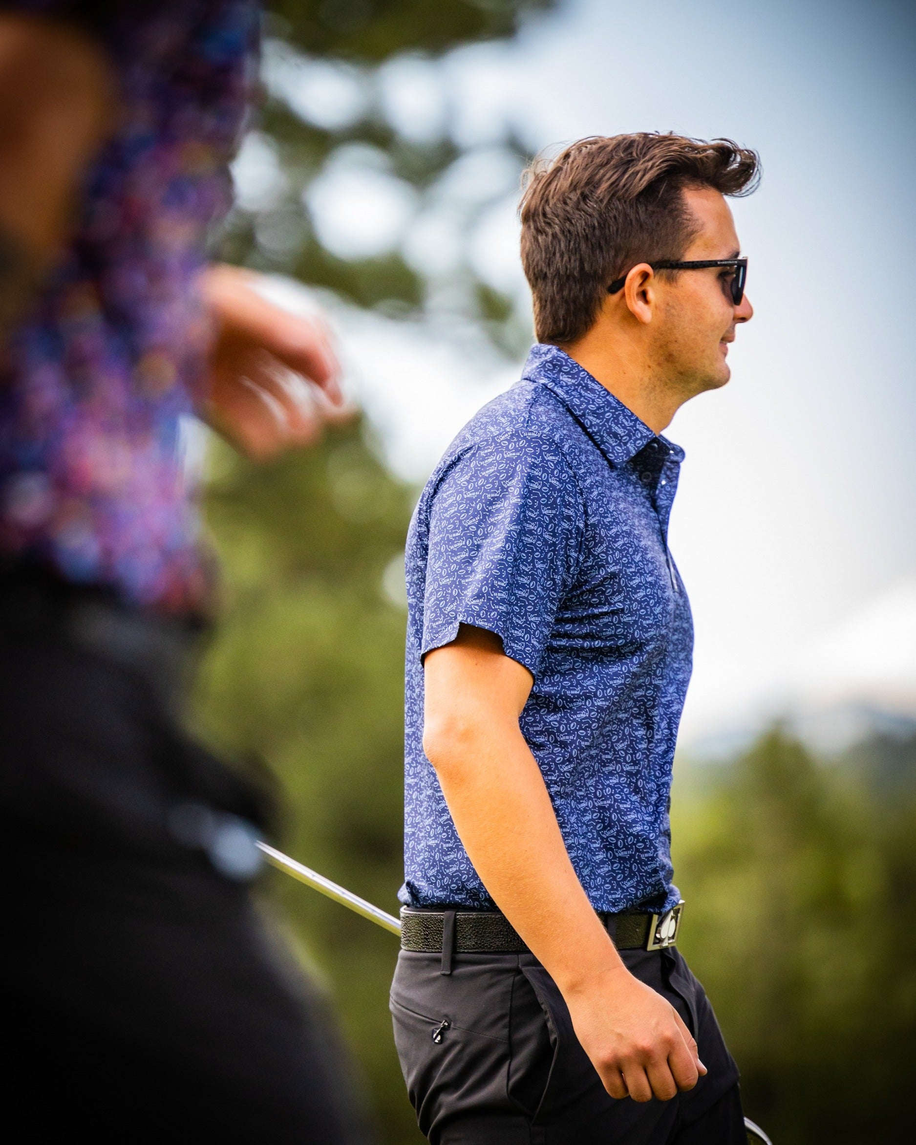 A golfer wearing a stylish blue patterned polo shirt walks confidently on the course, showcasing bold golf fashion.